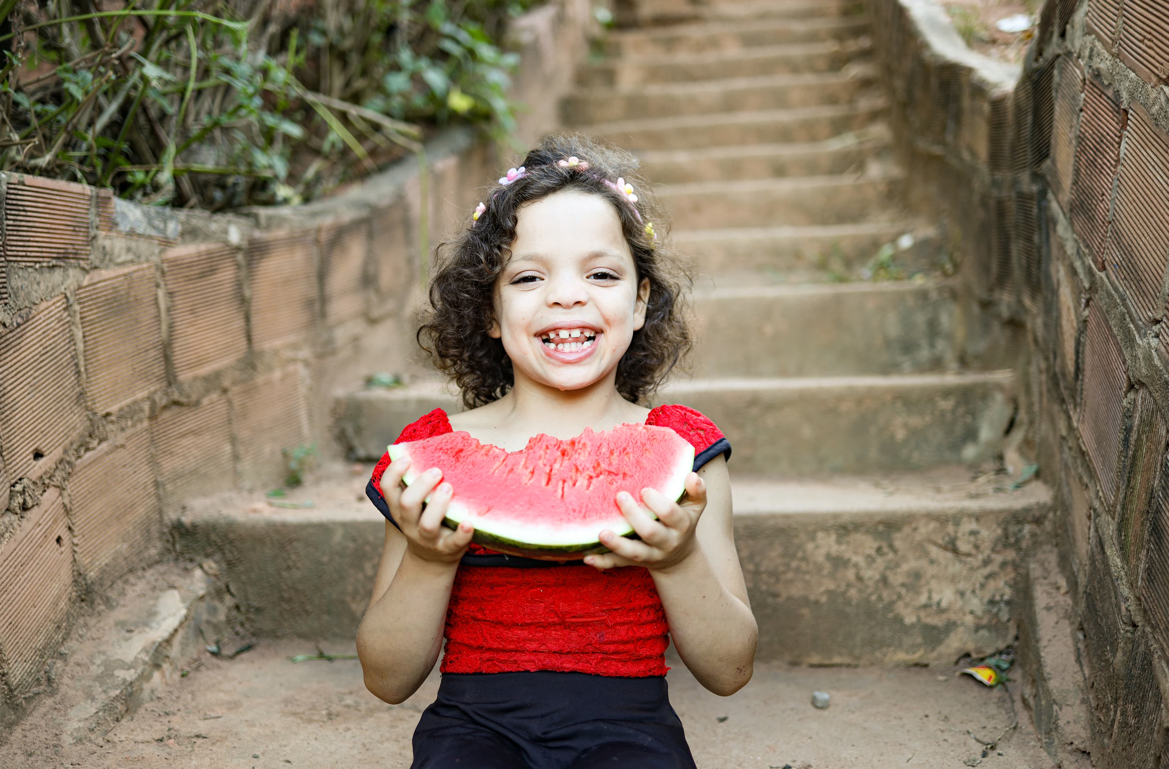 A young girl smiles brightly while holding a slice of watermelon.