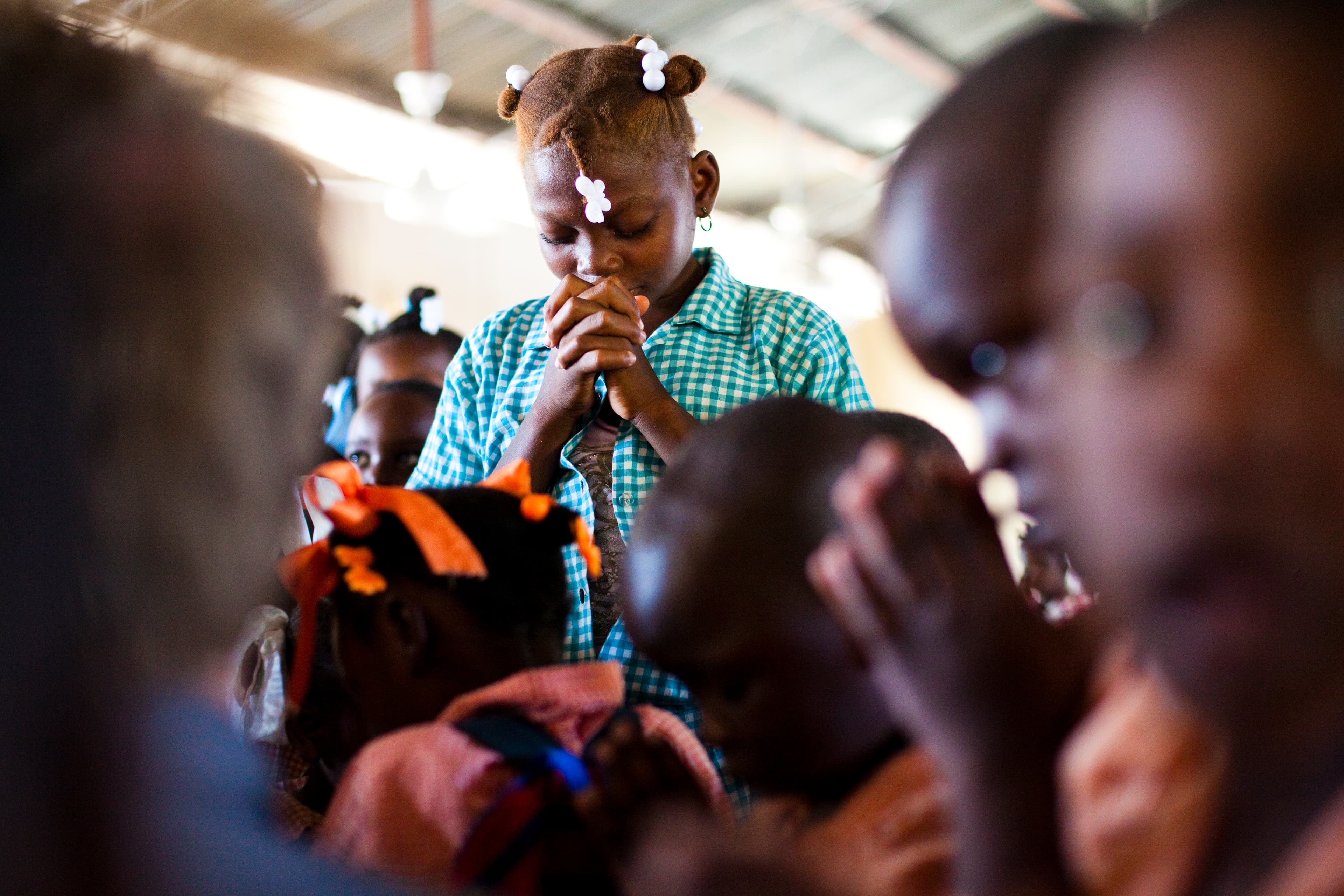 Young girl stand in a crowd alone praying with her eyes closed.