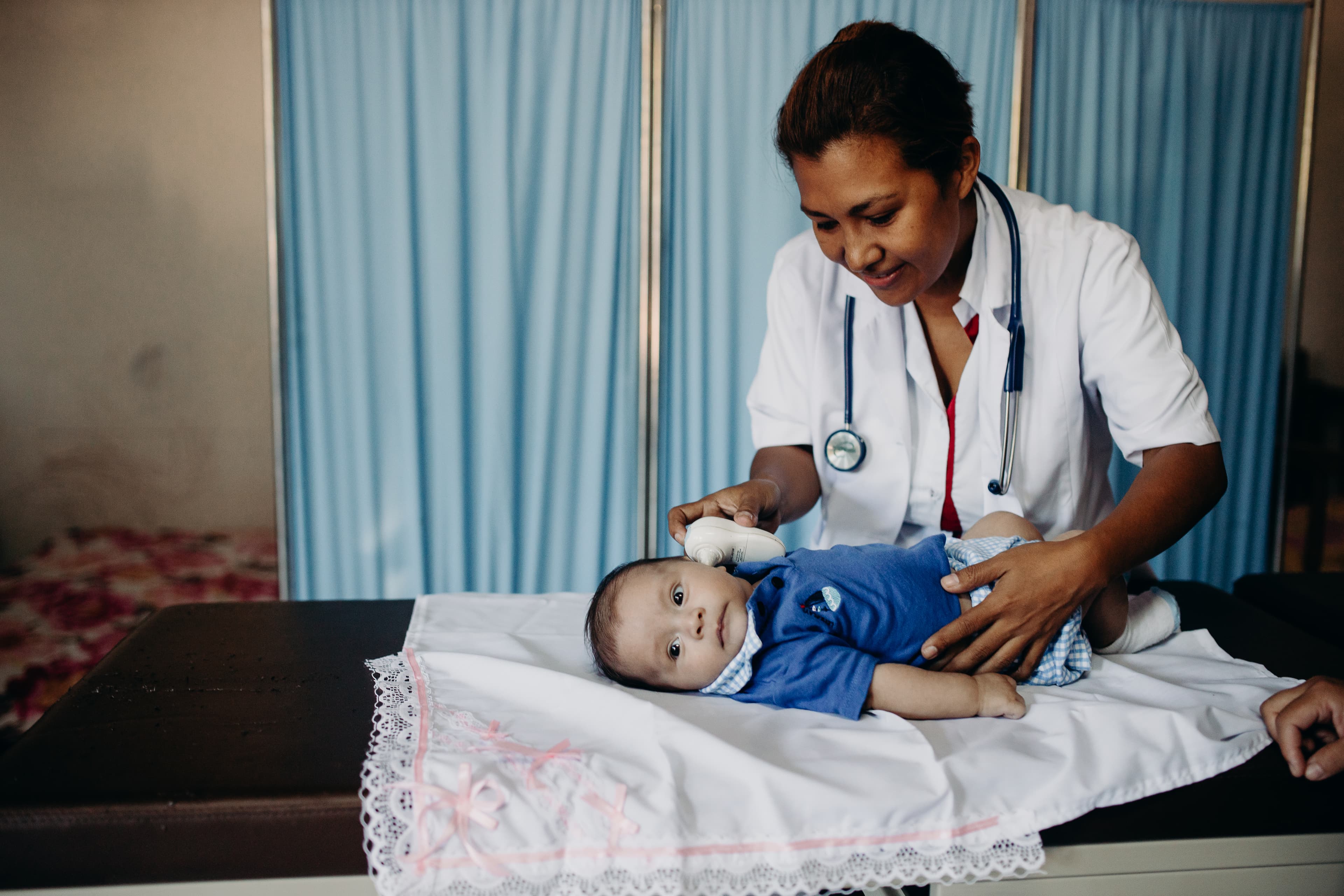 A doctor checks the temperature of a baby boy who’s lying on a medical table.