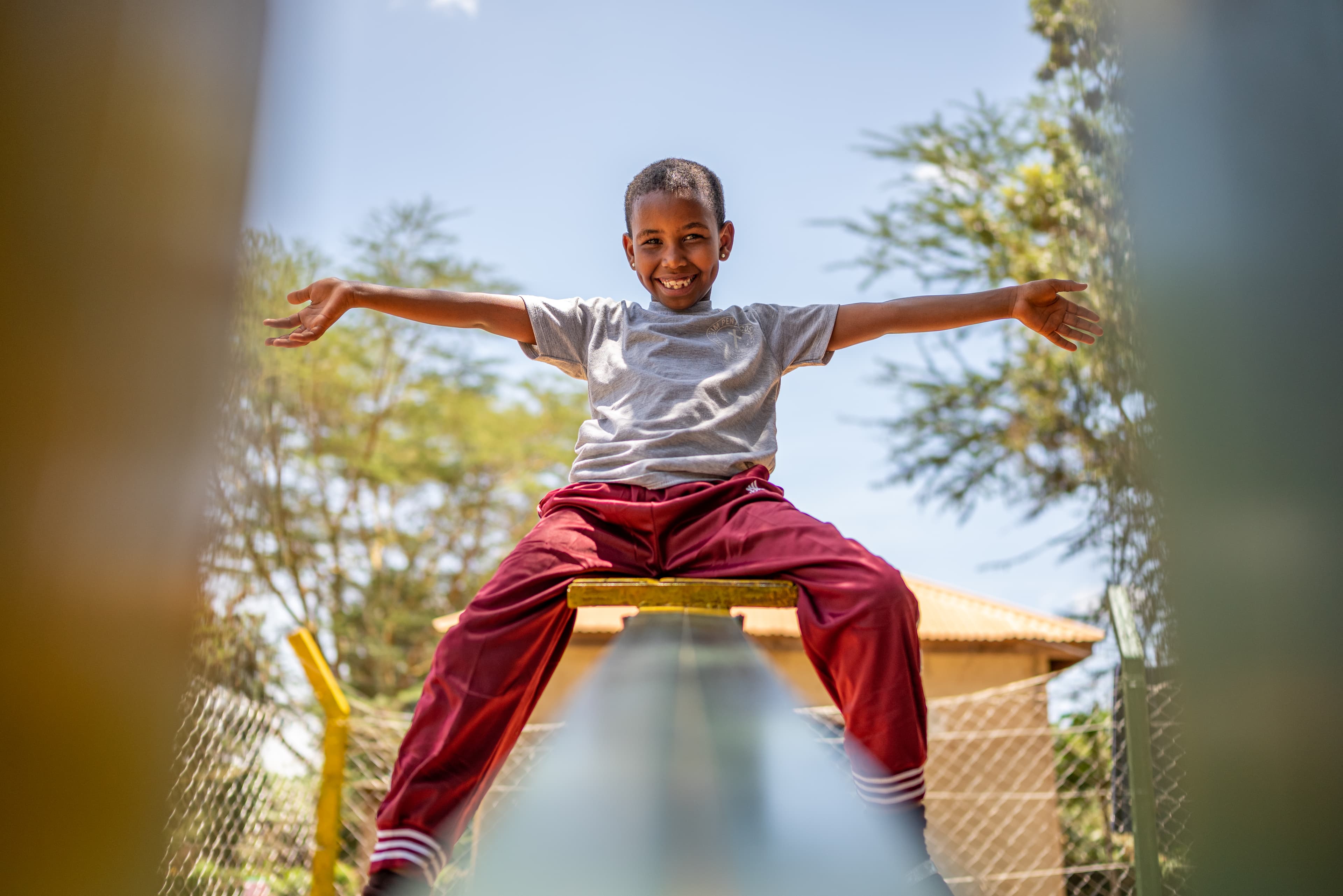 A young boy throws his arms in the air at the playground on a see-saw.