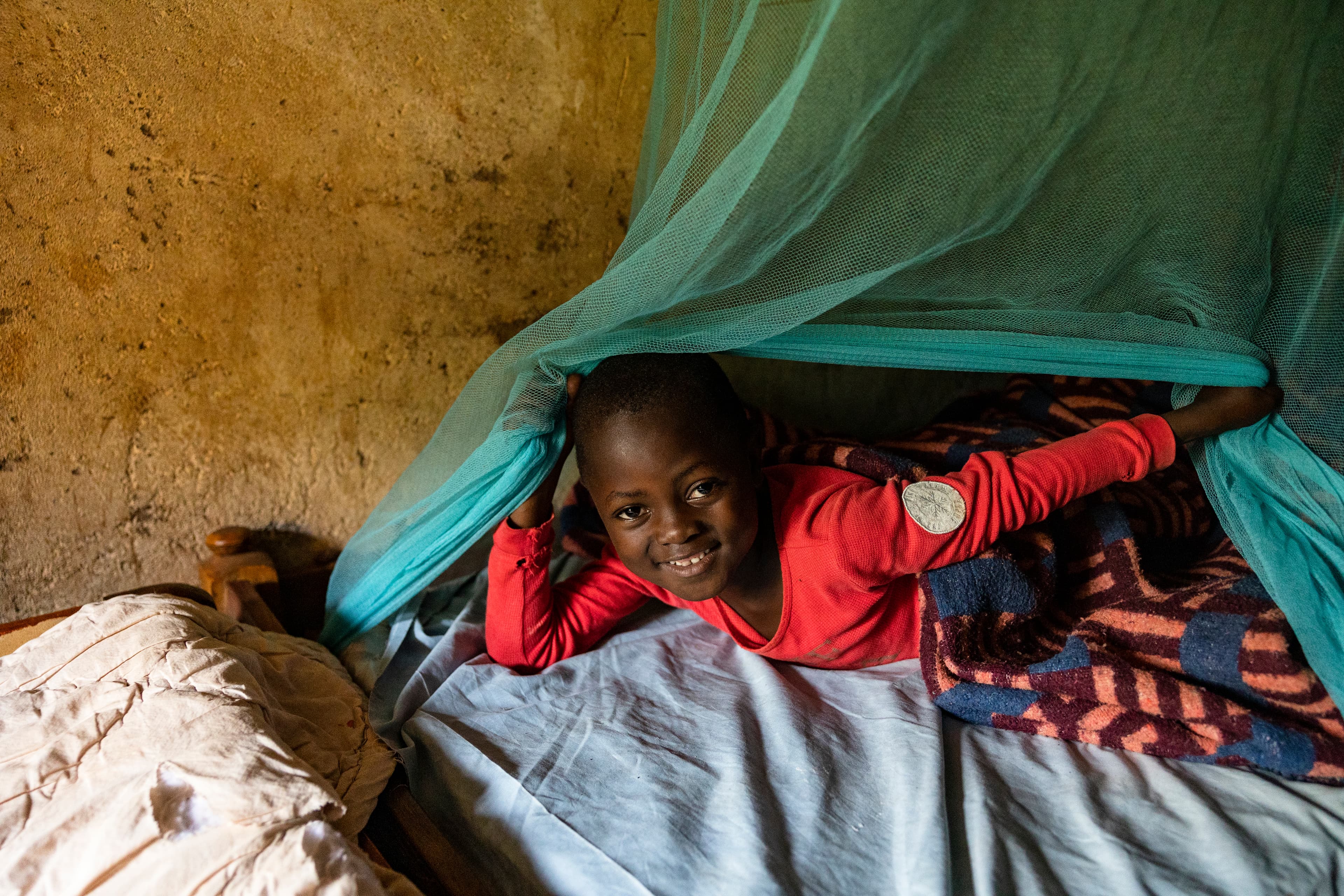 A young African boy lays on his bed under a green mosquito net.