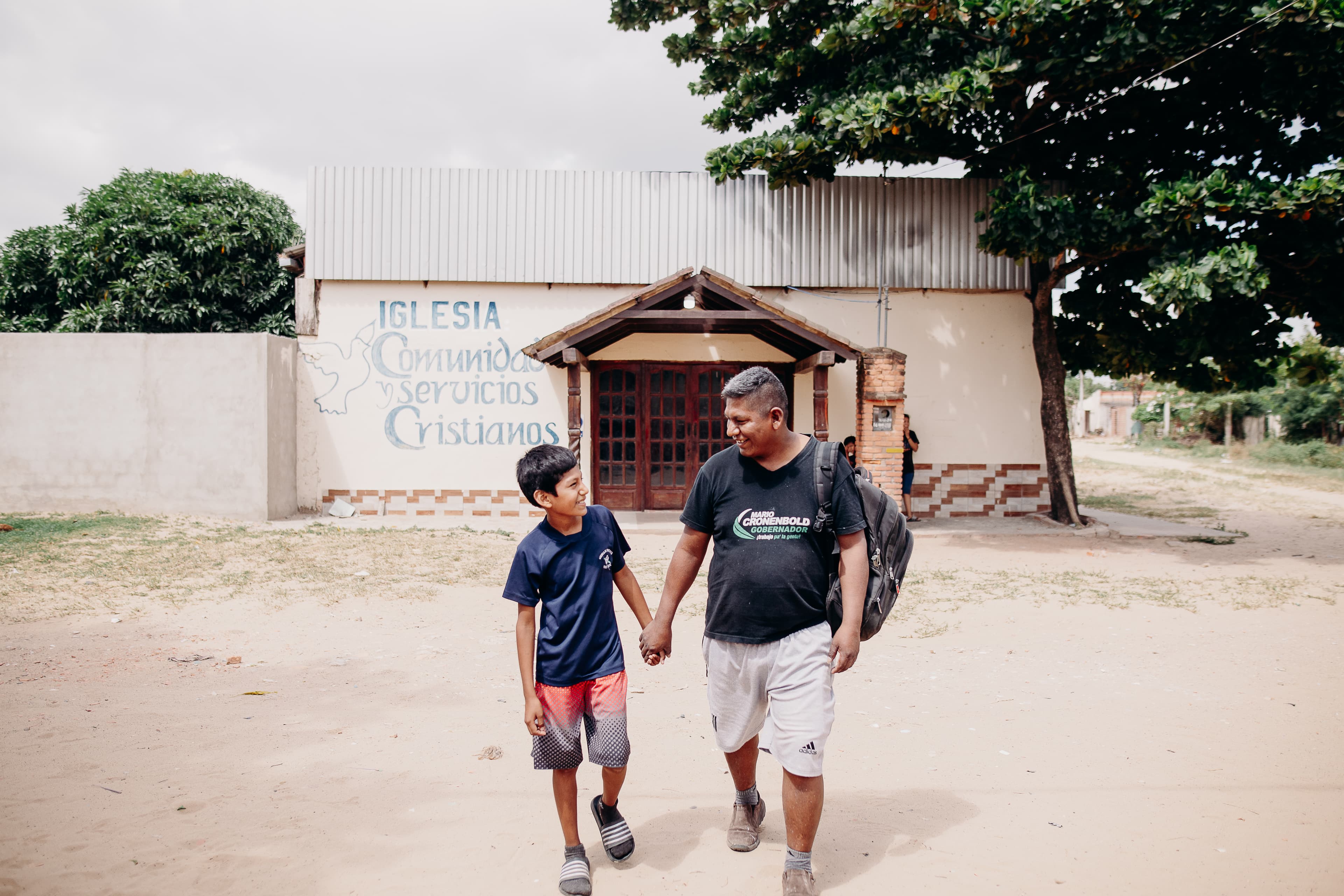 An older man and young teen boy hold hands and walk in front of a church.