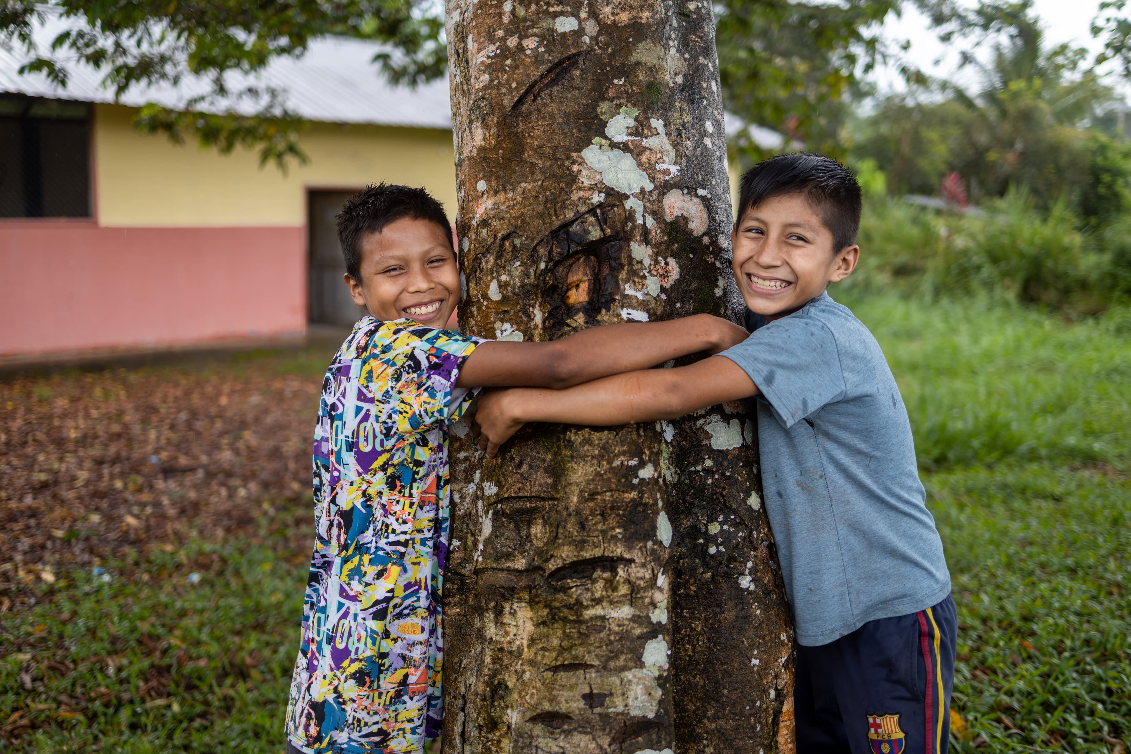 Two boys embrace a tree while smiling for the camera.