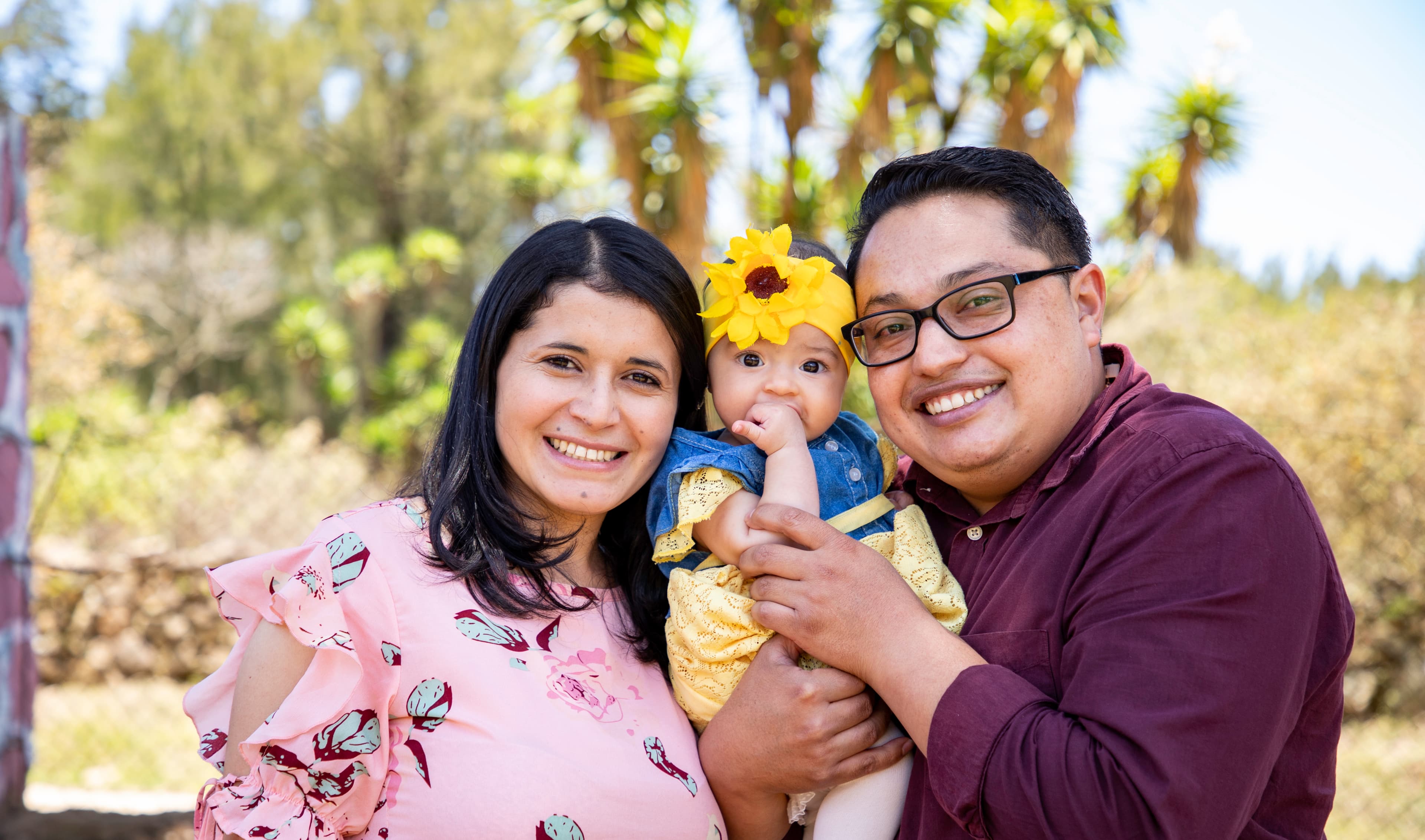A mother and father are smiling and holding their daughter in between them.