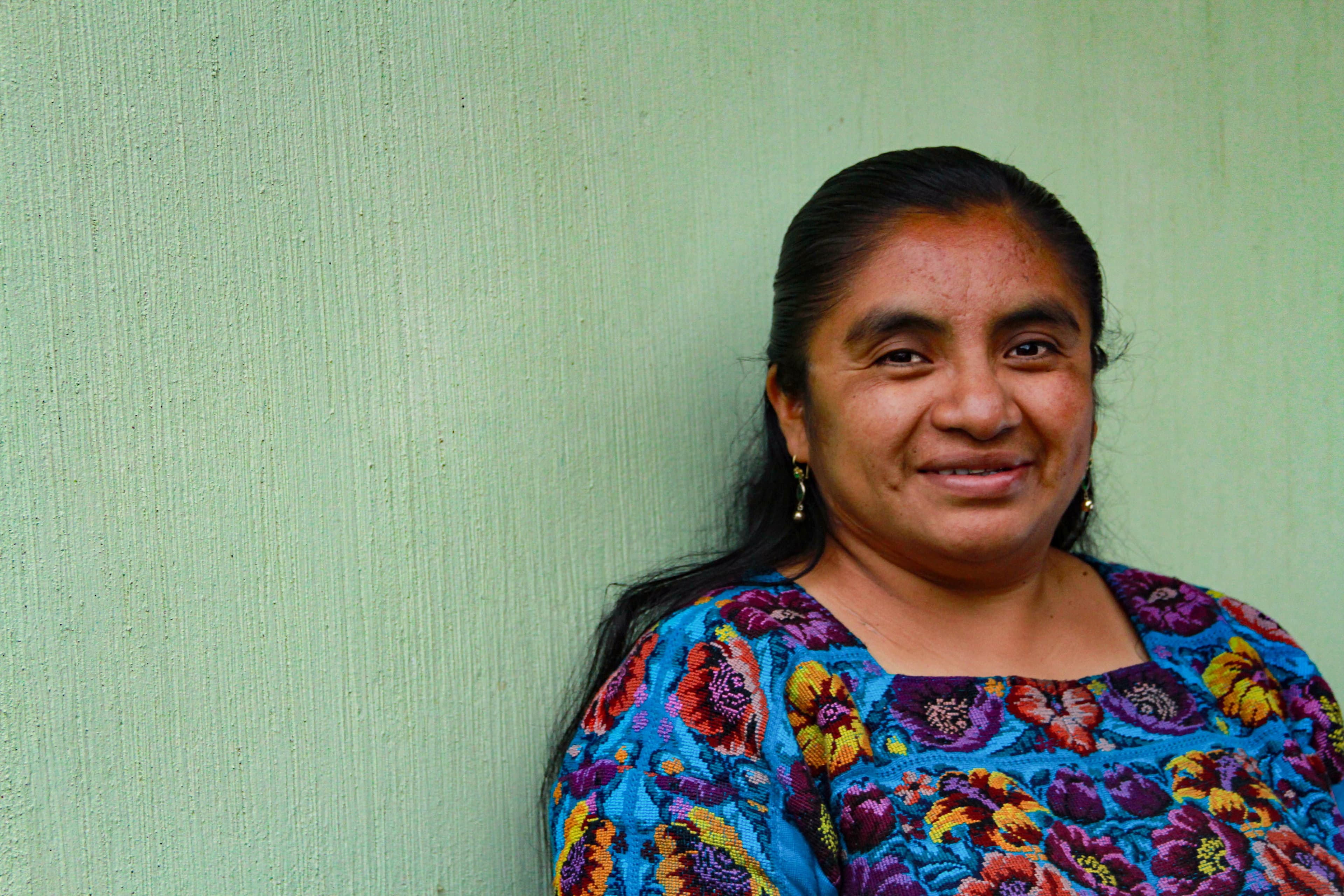 Bianca is leaning against a green wall and smiling at the camera.