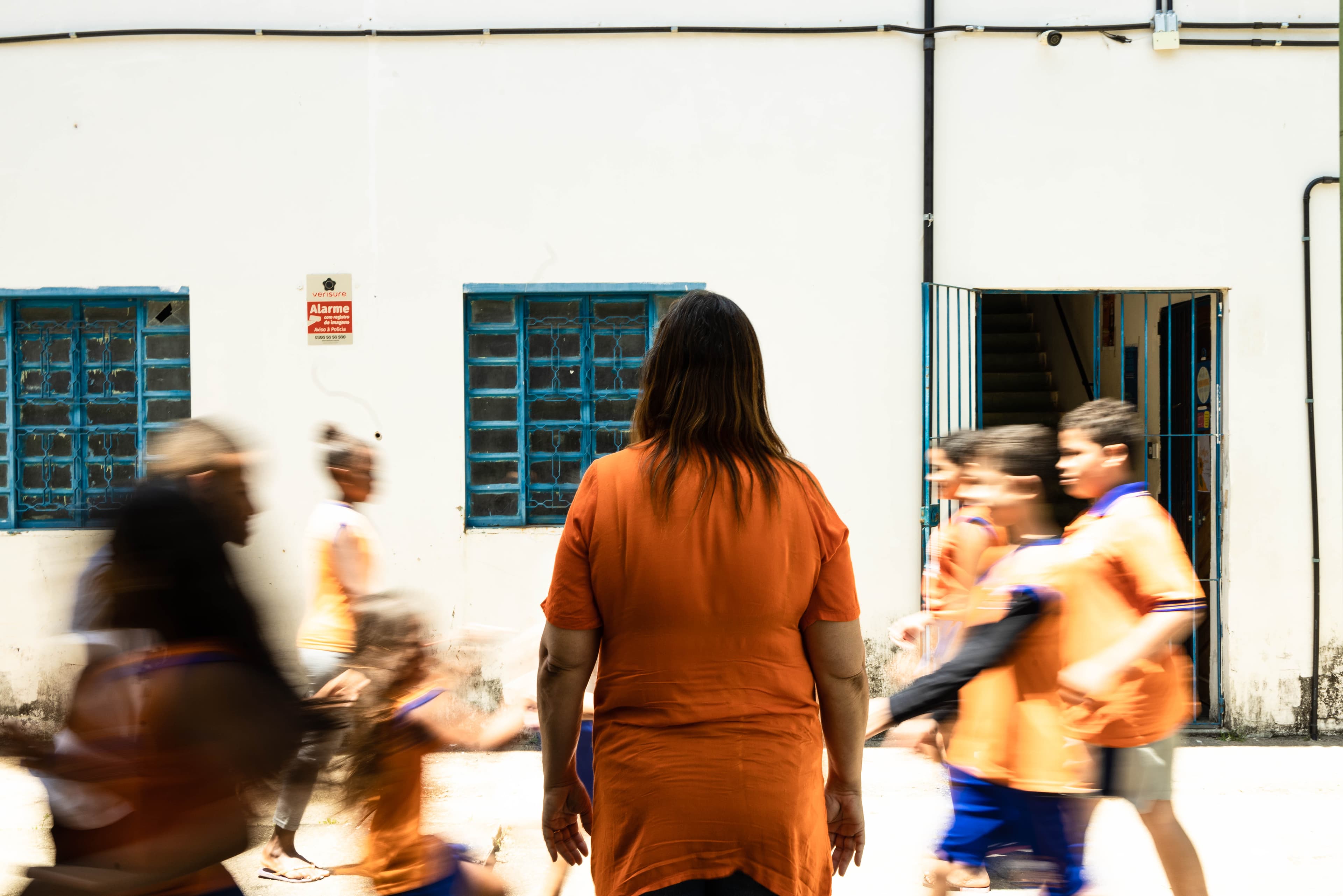 An older woman wearing a bright orange shirt stands with her back to the camera.