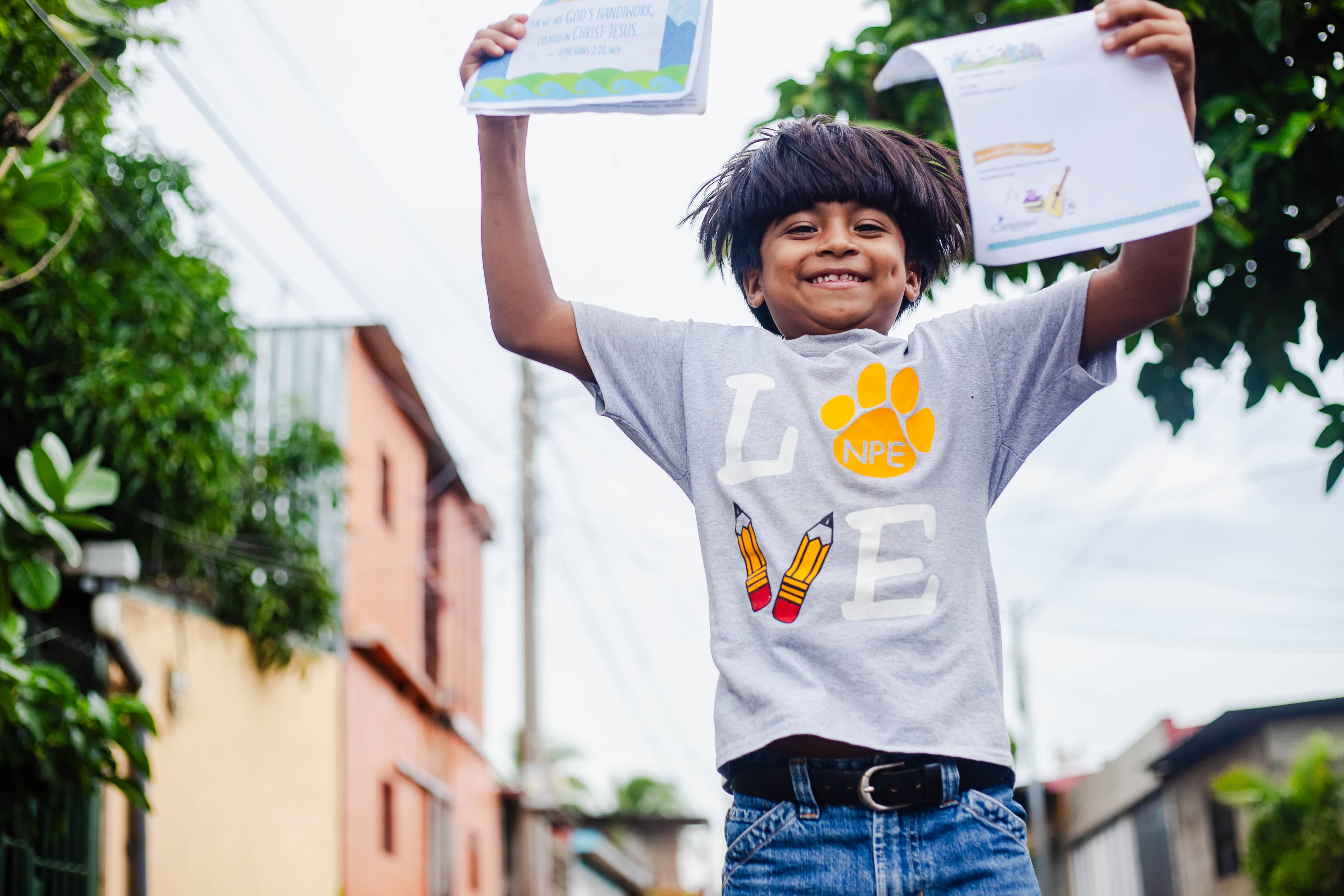 A young boy jumps into the air while holding two letters in his hands and smiling.