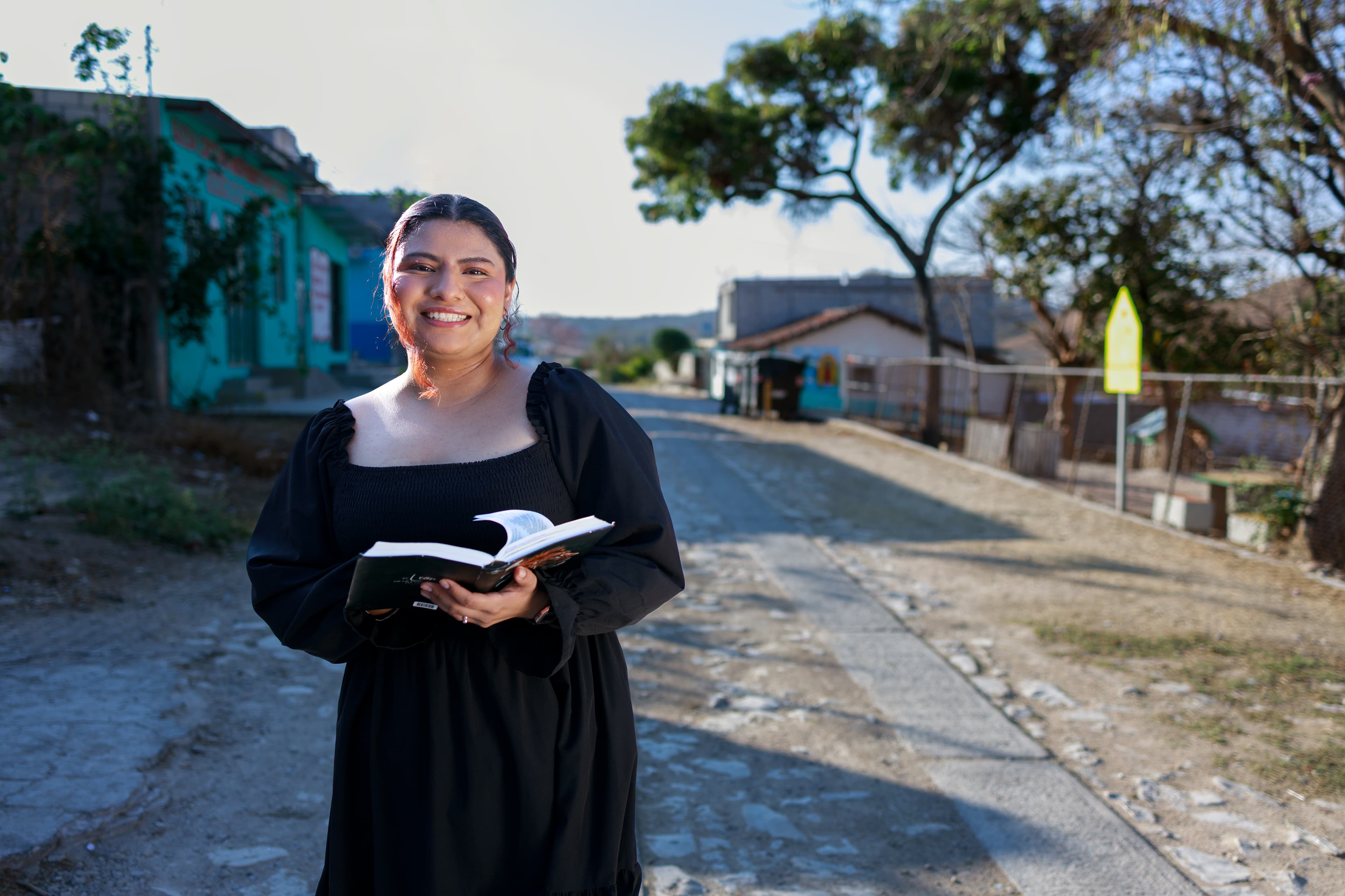 A young woman is holding a bible in her hands and smiling.