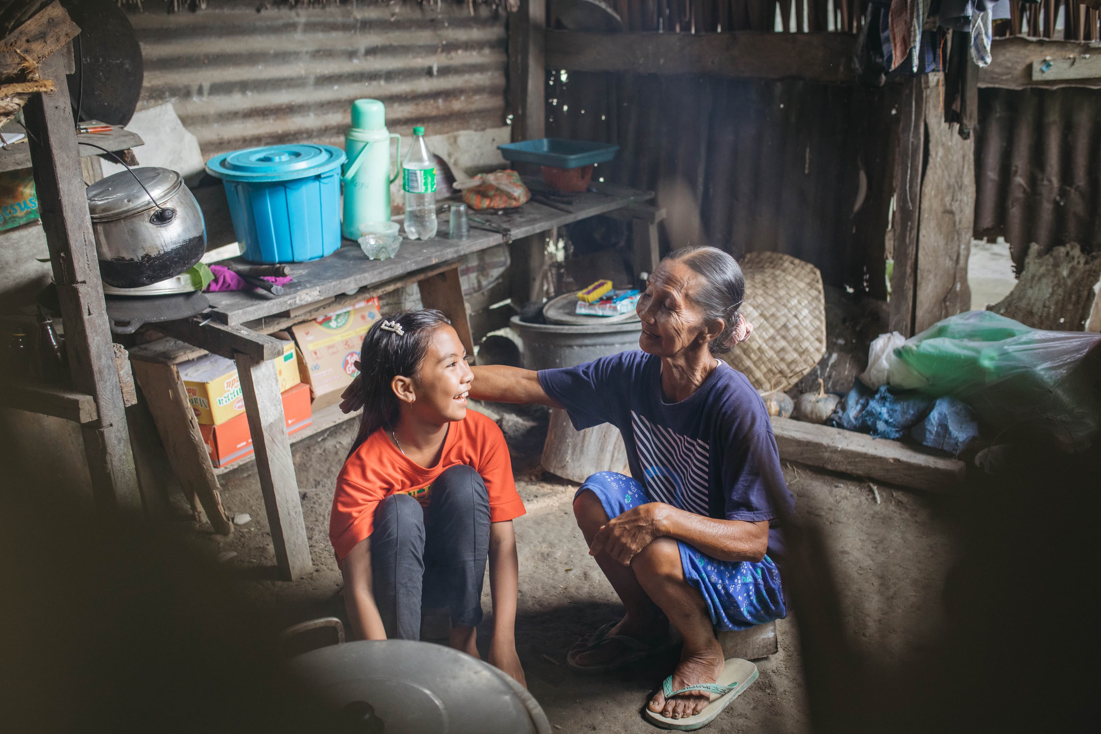 A young girl and her grandmother sit together in their home smiling.