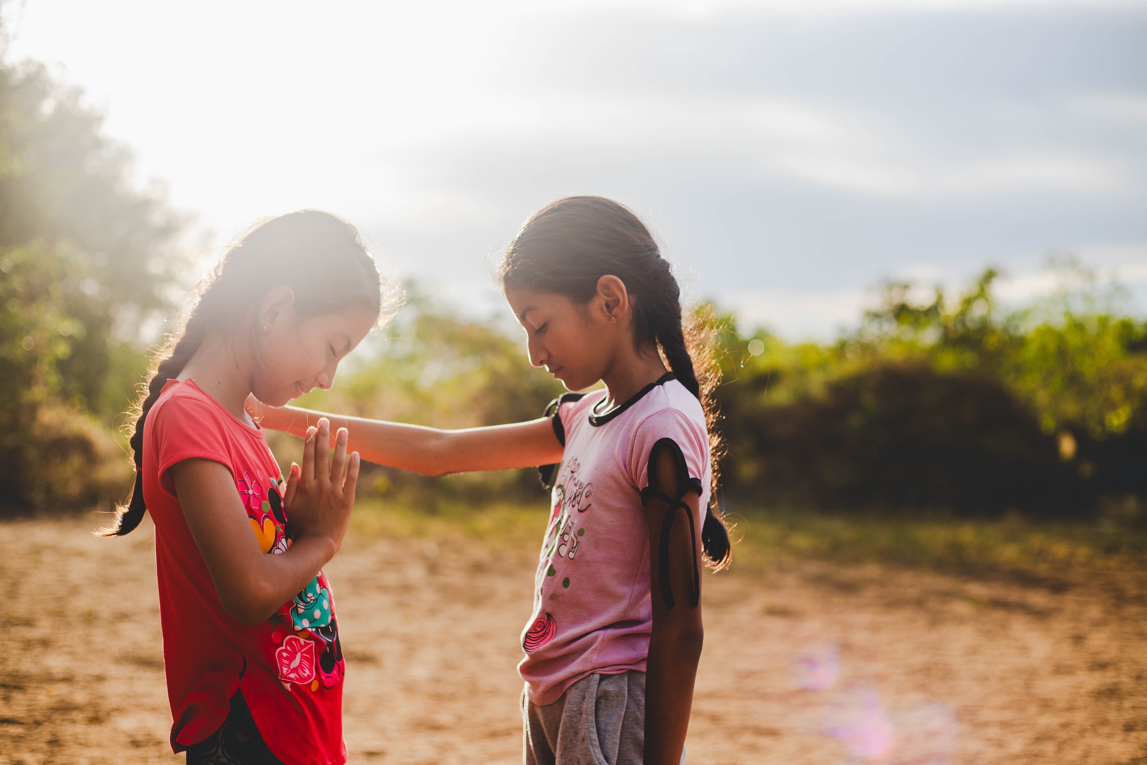 Two young girls are praying together with their heads bowed.