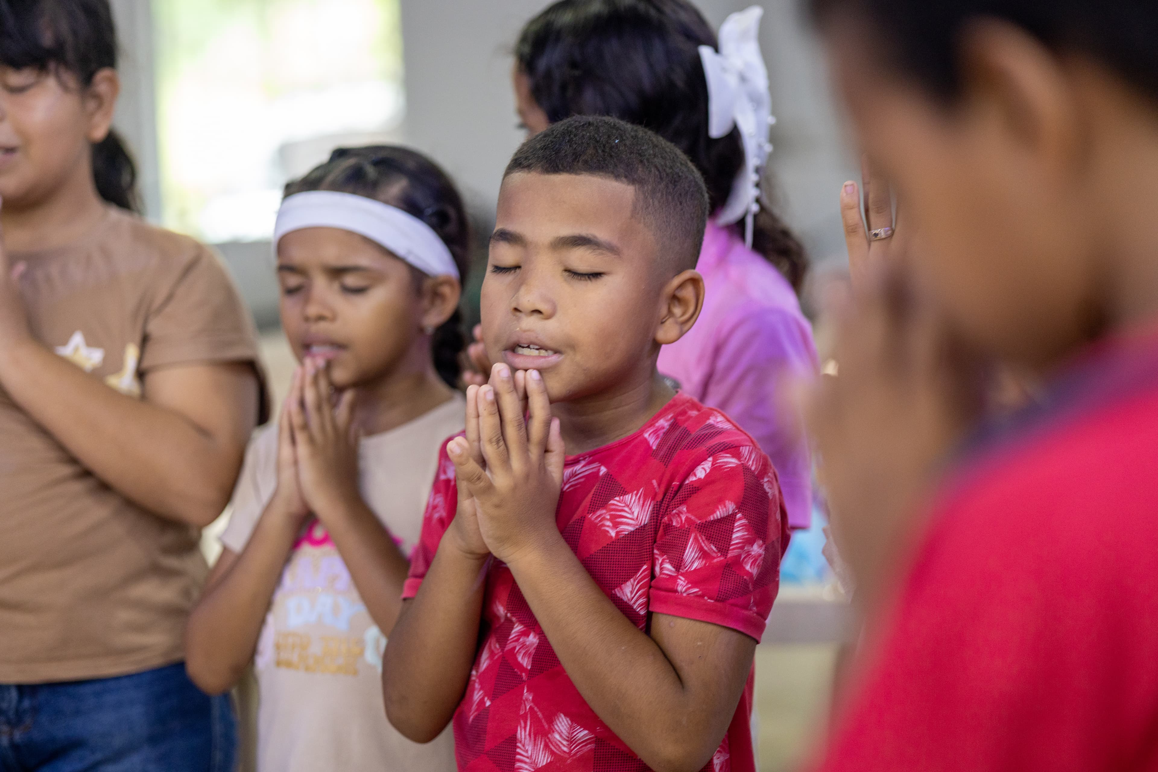 A group of Colombian children fold their hands and close their eyes in prayer.