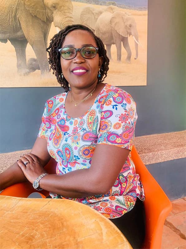 A portrait of Doreen sitting down at a desk and wearing a brightly patterned shirt.