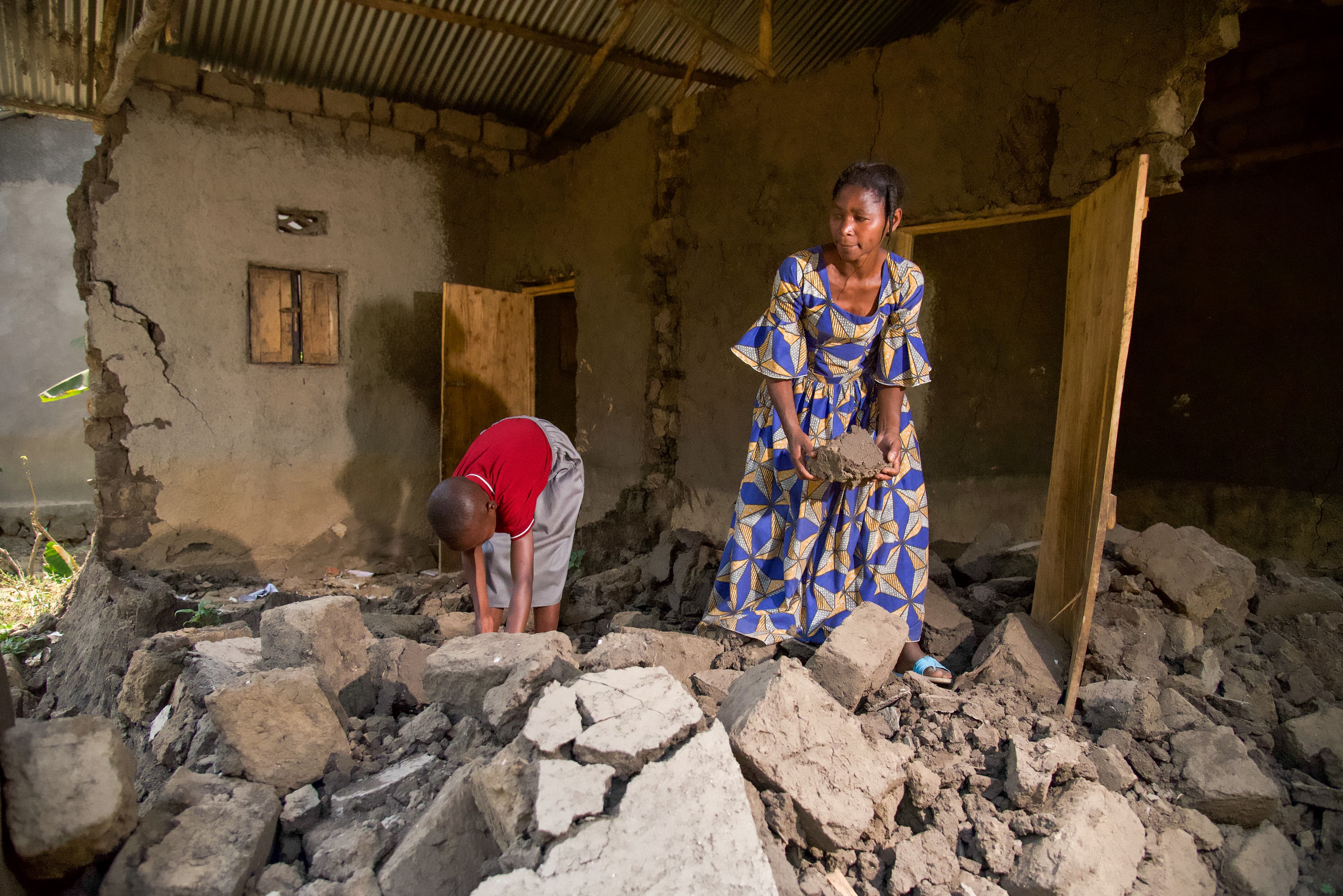 A young boy and his mother work to pick up large concrete blocks after their house was destroyed.