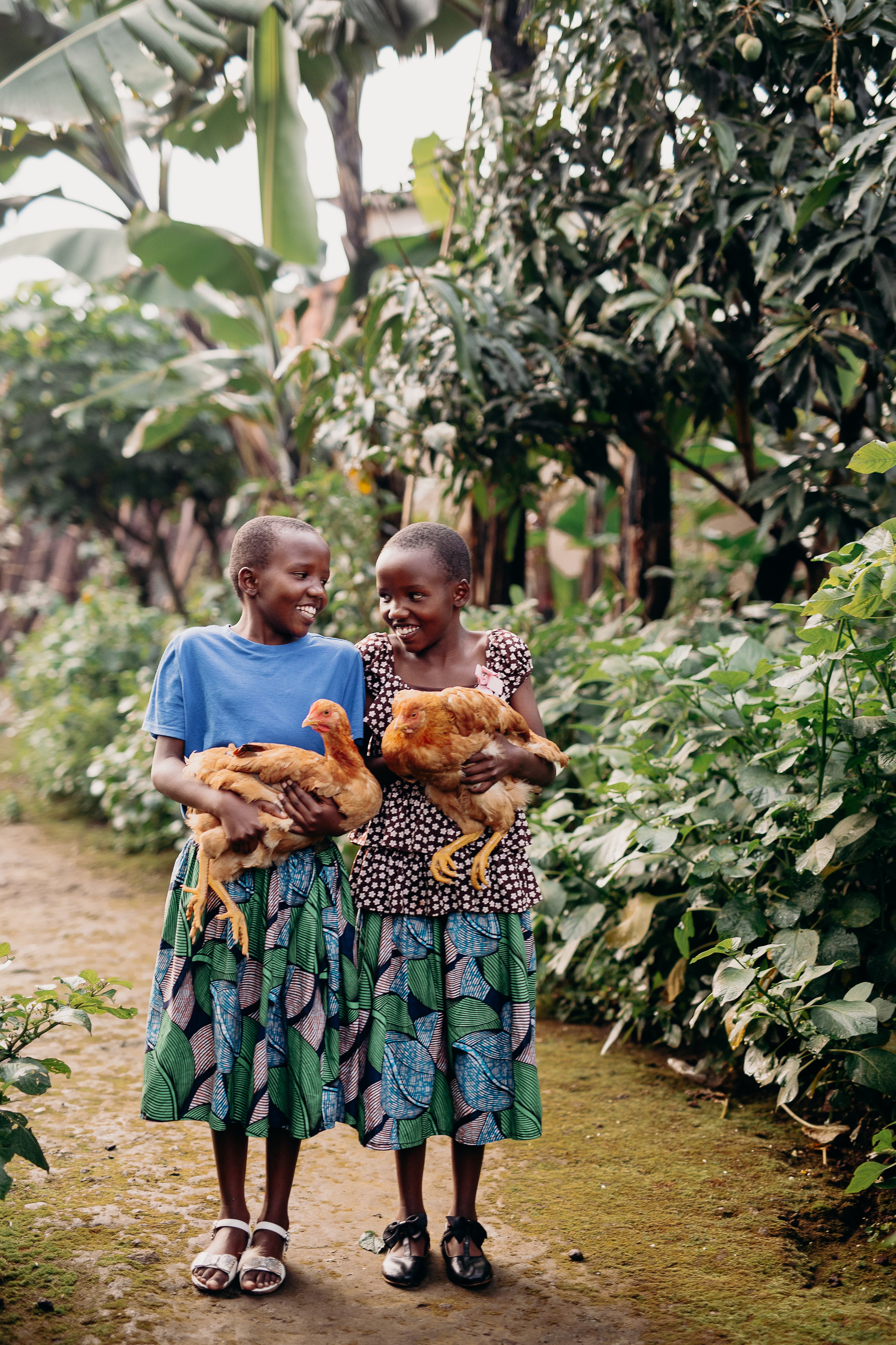 Two girls smile at each other, both holding a chicken.