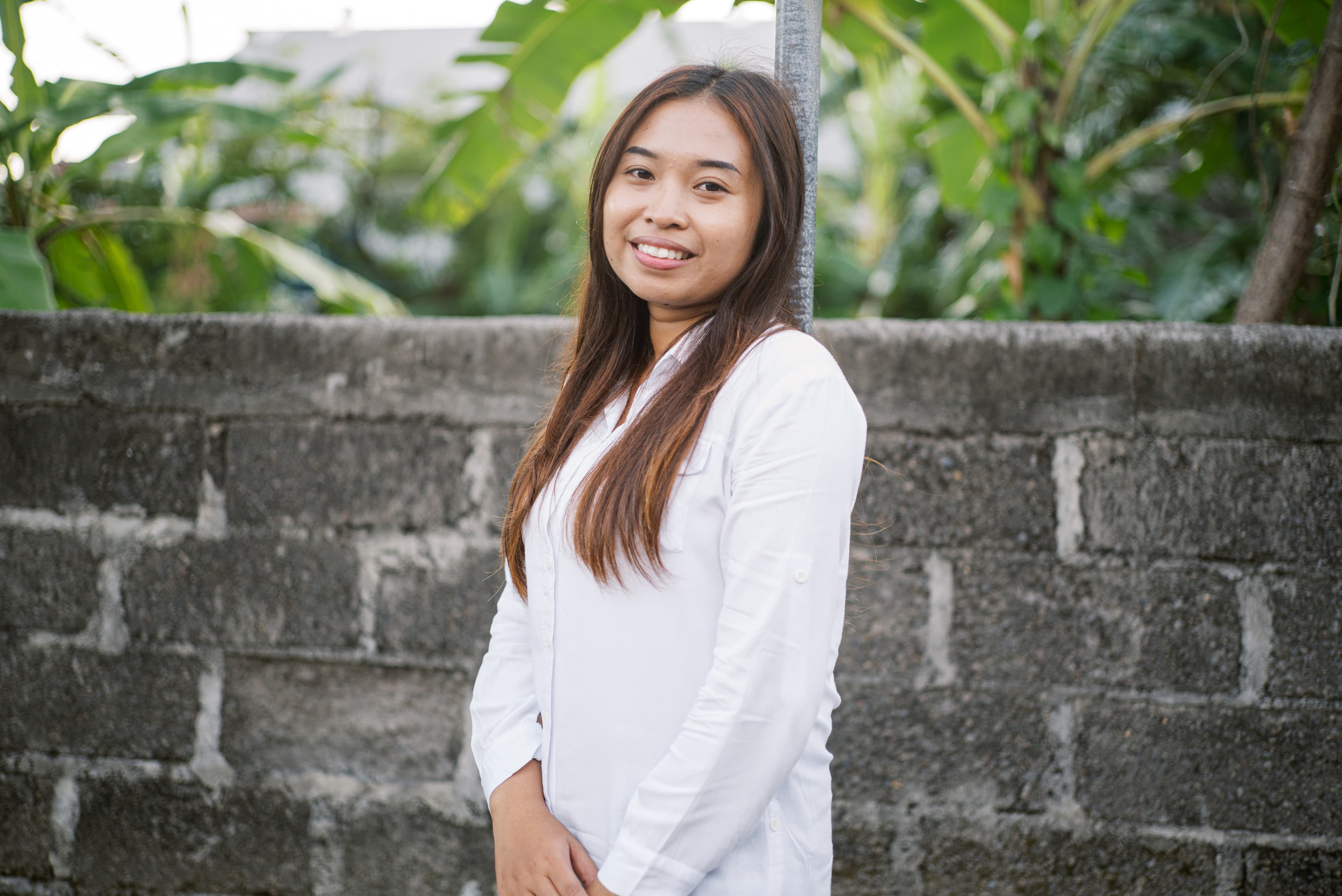 A teen girl stands in front of a brick wall wearing a white lab coat and smiles.