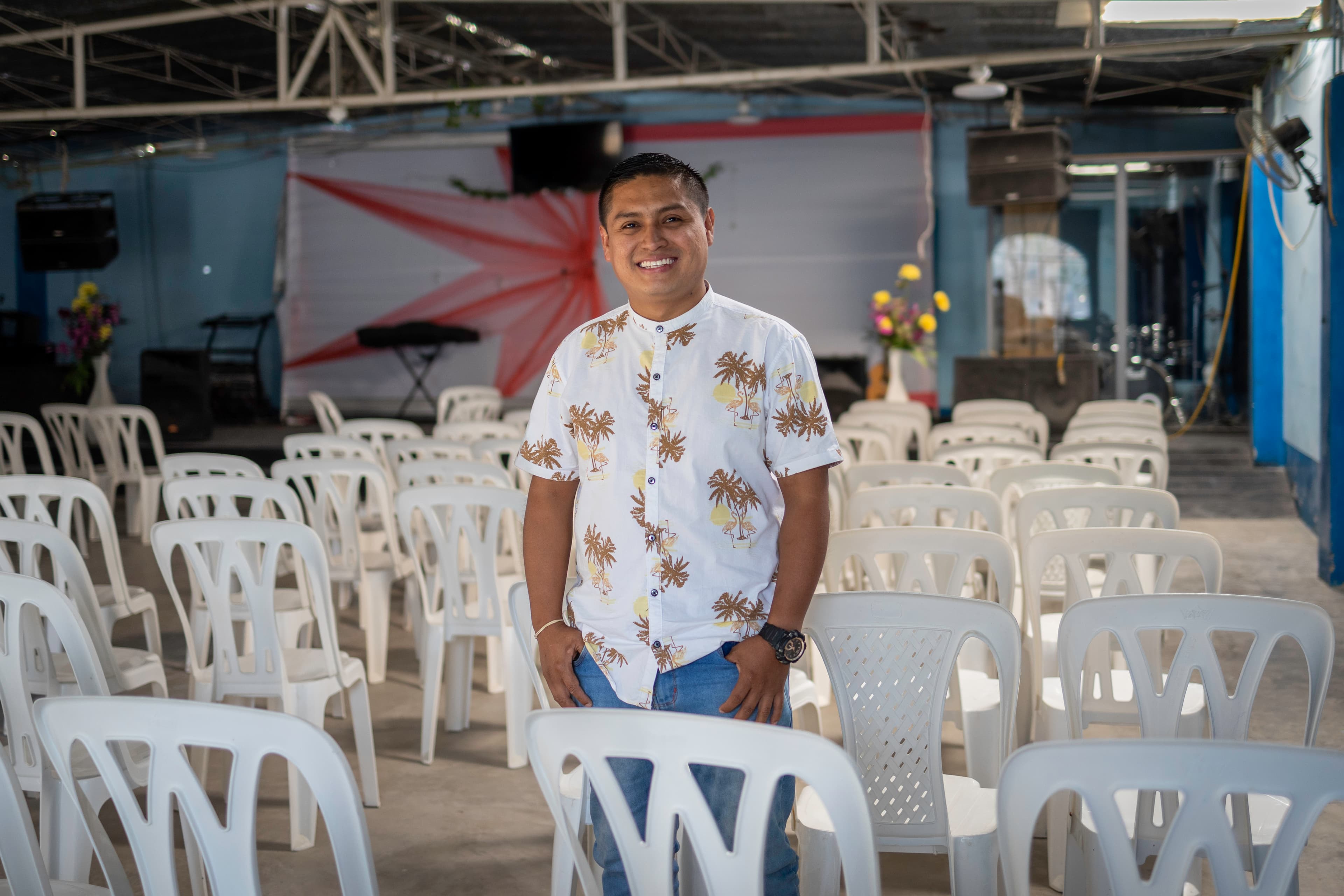 A man is standing confidently and smiling inside the church where he serves.