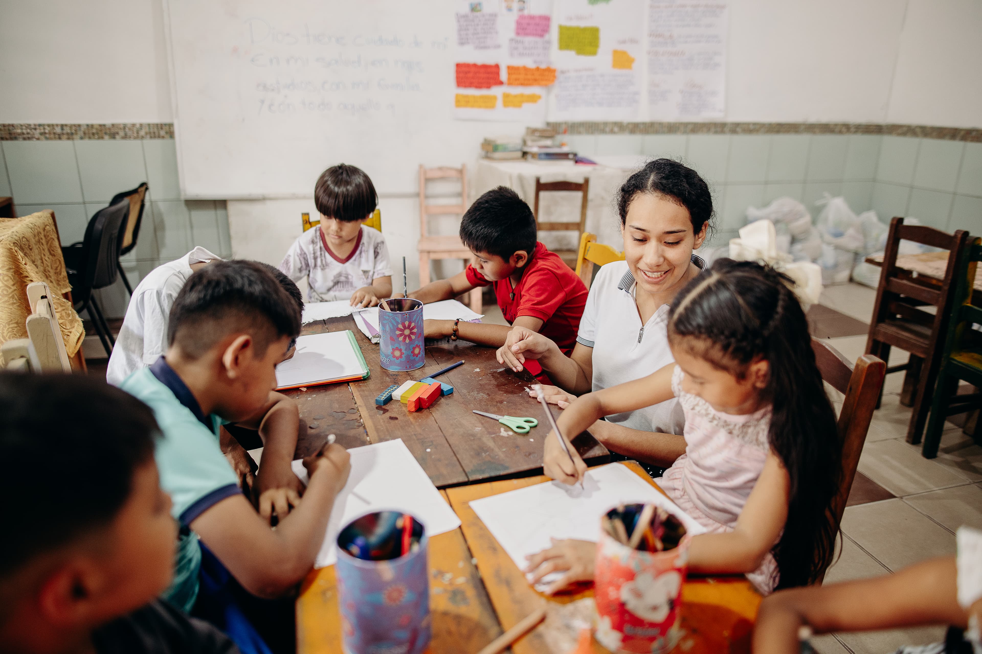 A teen Bolivian girl sits among a group of children at a table.