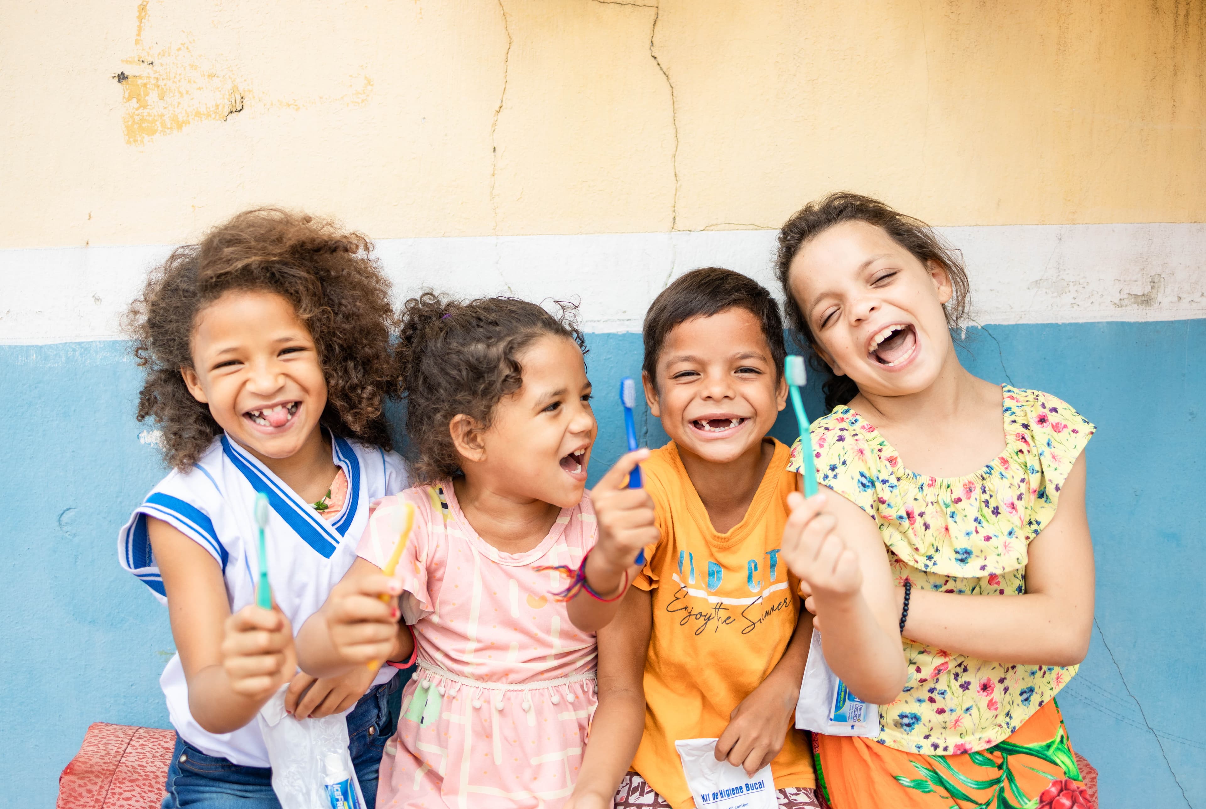 Four young children are holding toothbrushes while laughing and smiling.