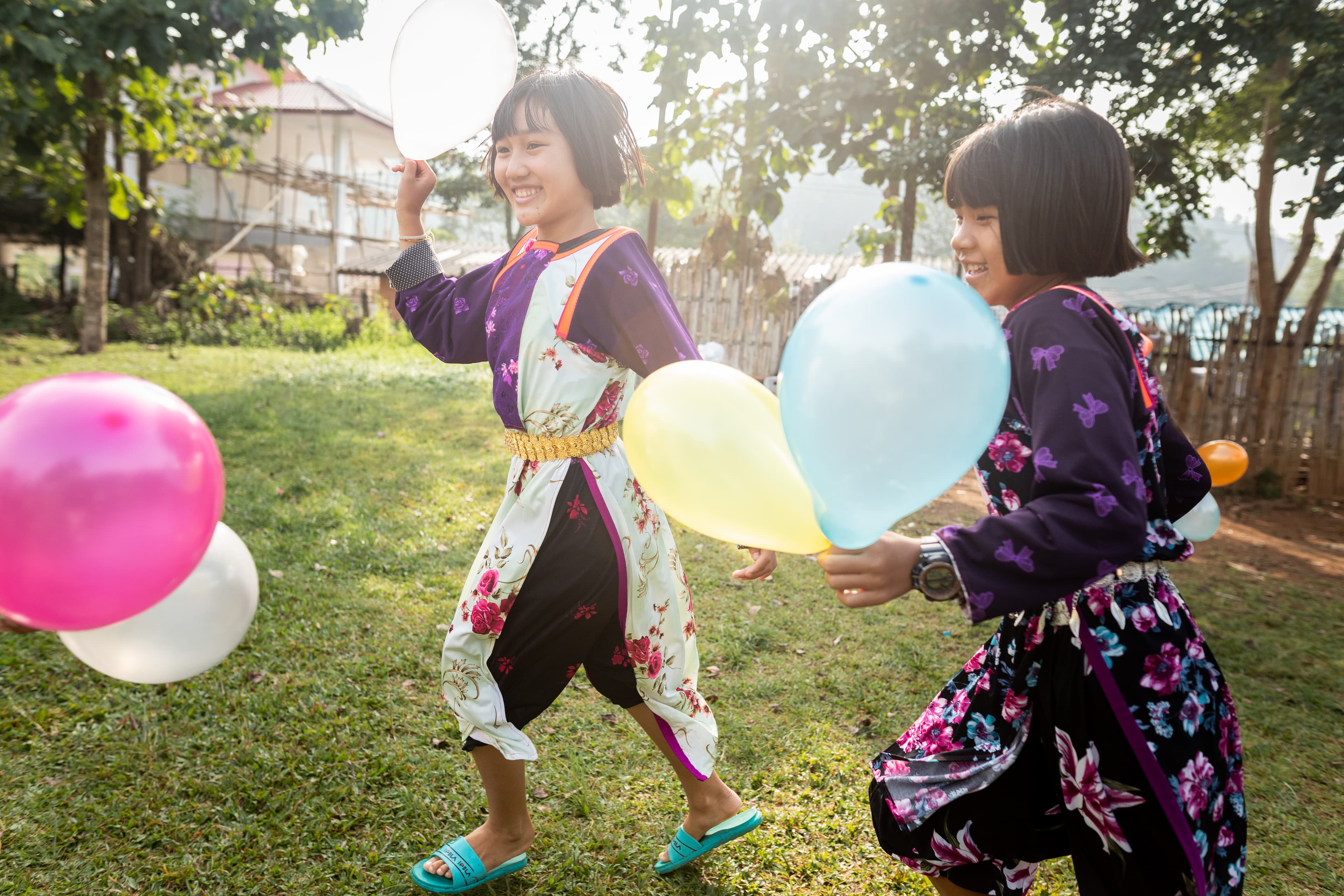 Two girls are smiling as they run and play with balloons.
