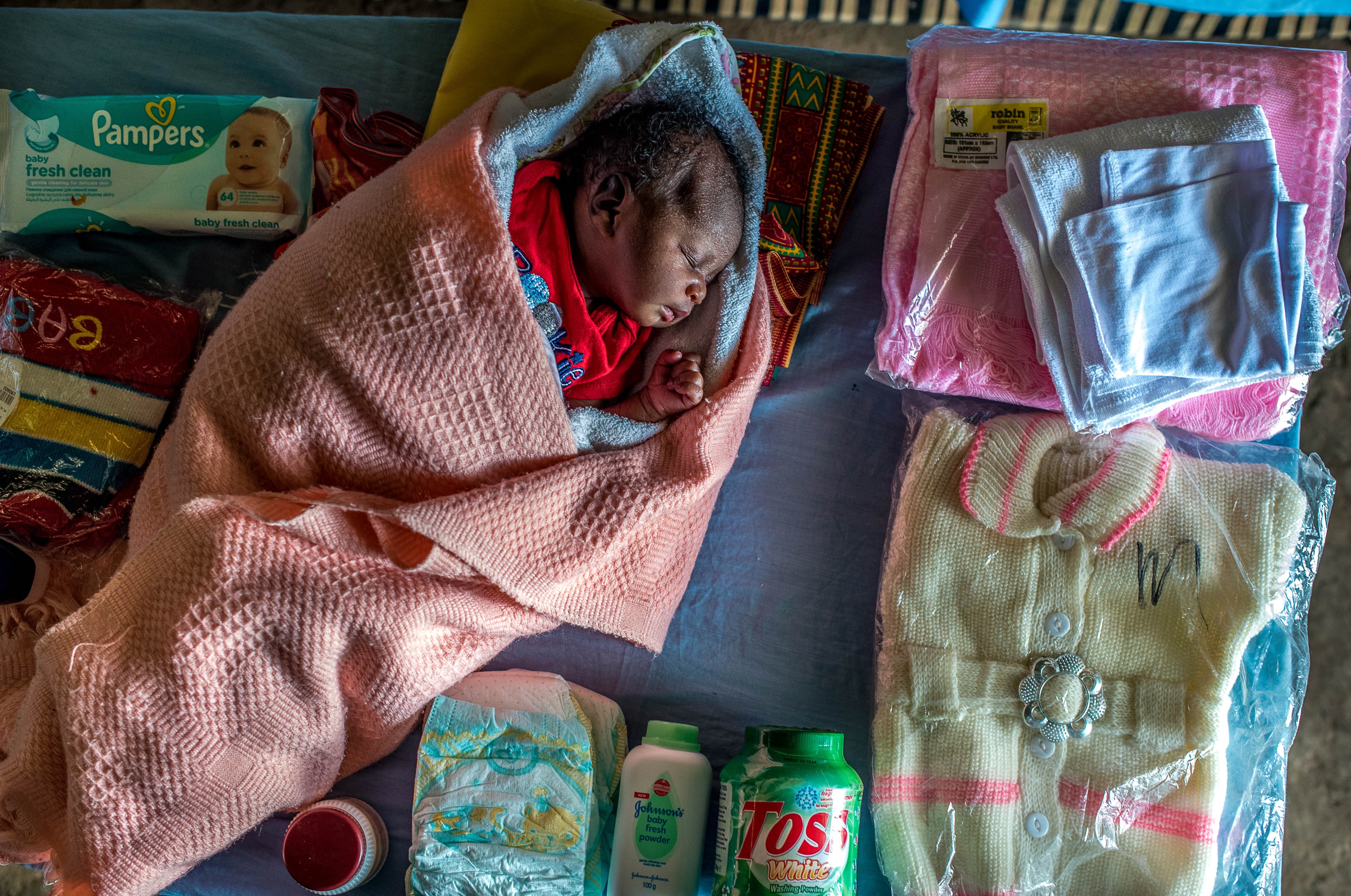 A baby sleeps next to a care package filled with basic supplies needed for newborn care.