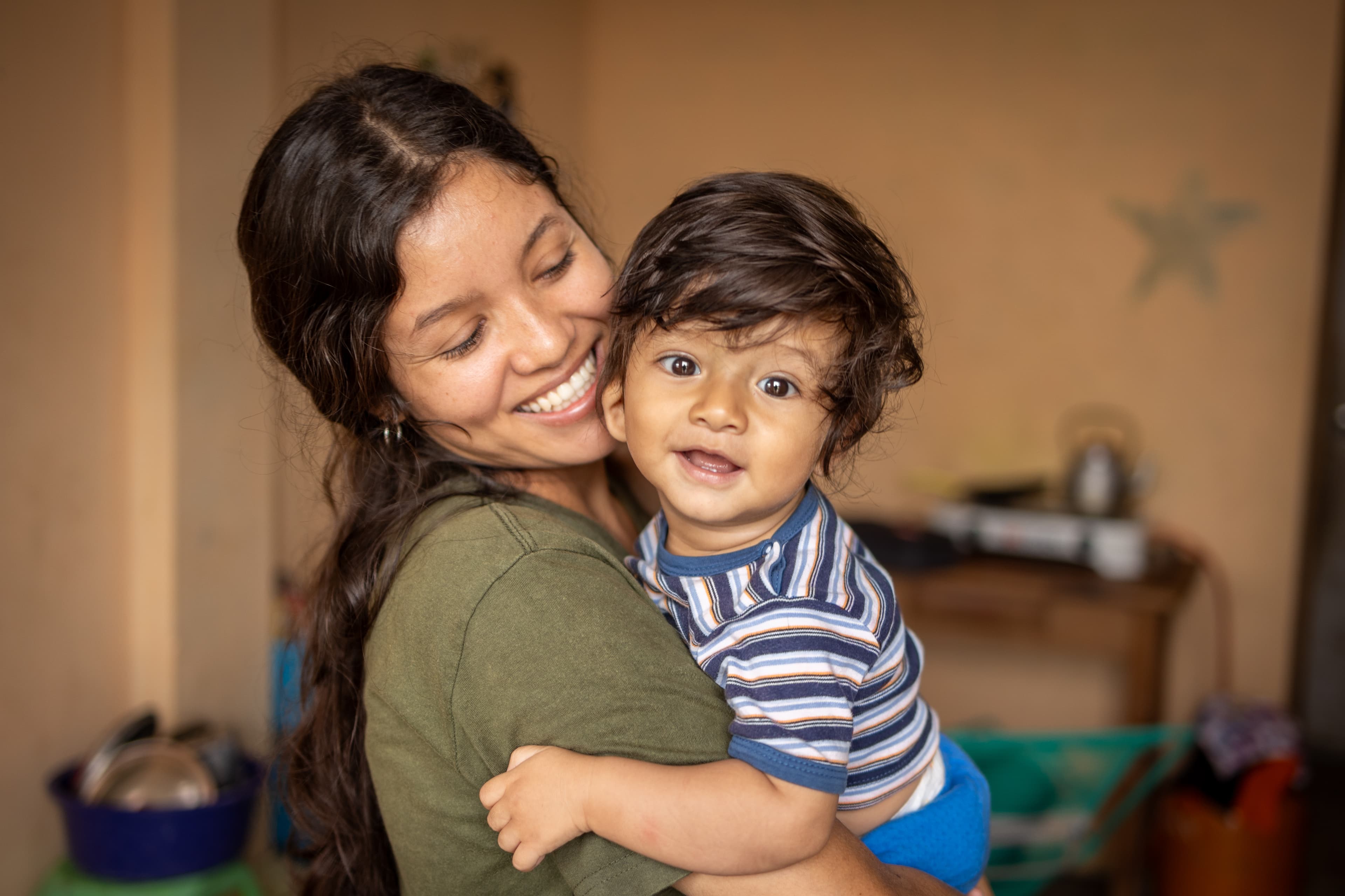 A mother is smiling as she holds her son in her arms.