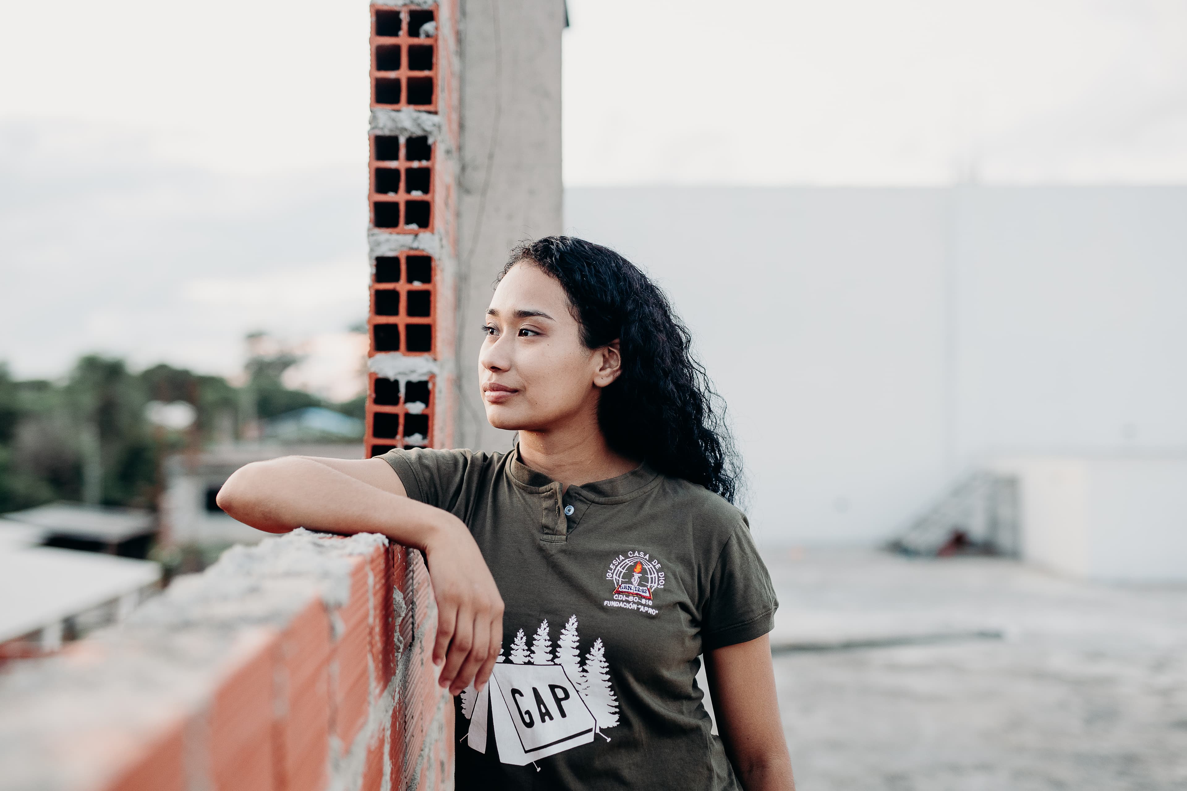 A teen Bolivian girl leans against a brick wall while looking to the right.