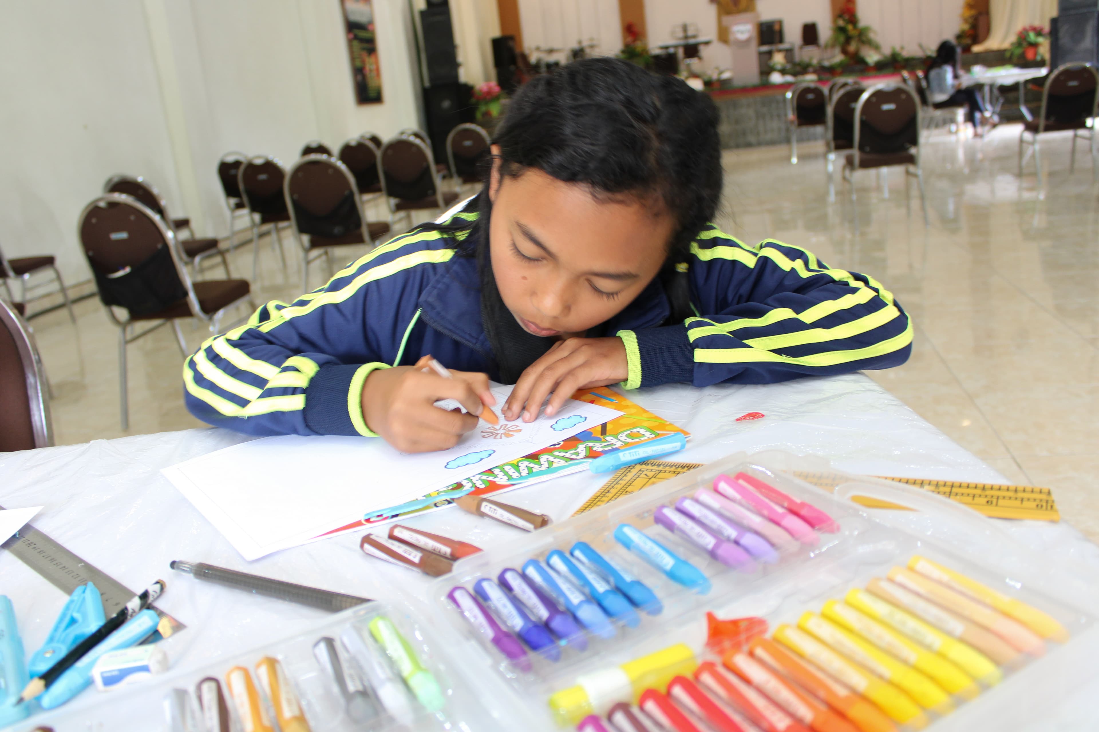 A young girl sits at a table coloring.