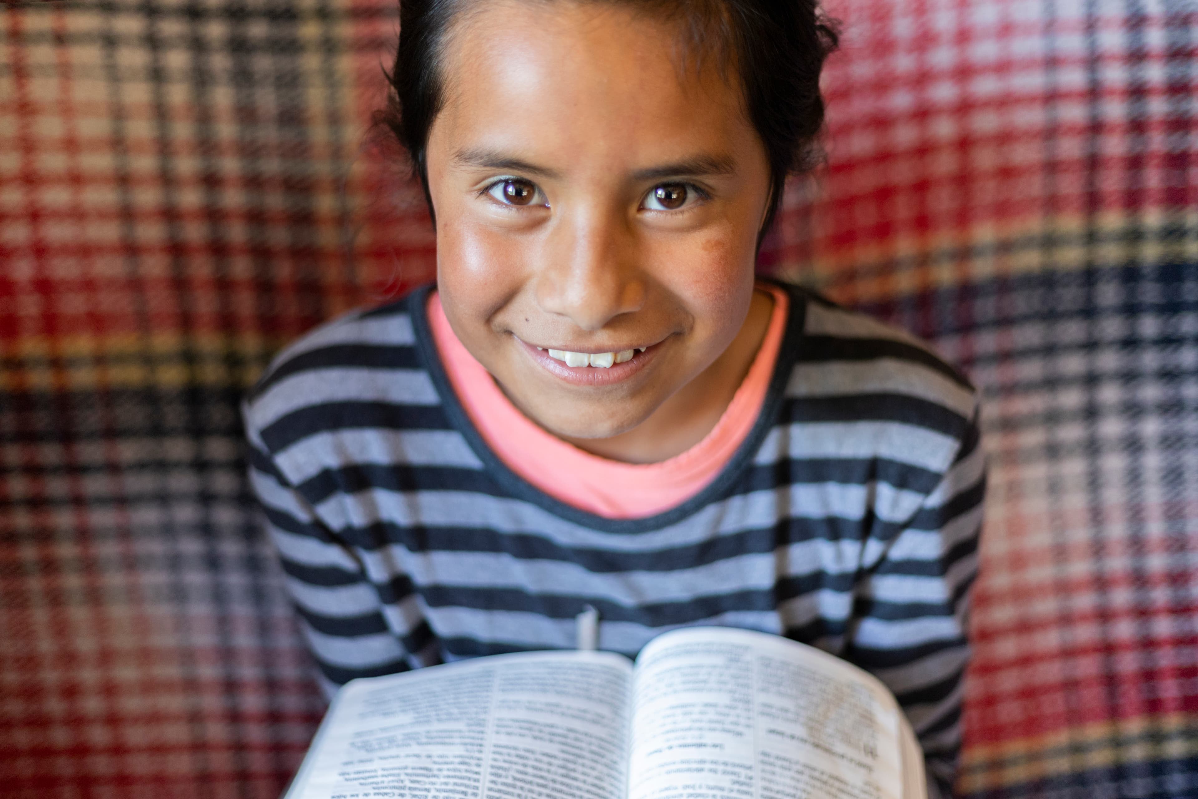 A young girl smiles at the camera while holding the Bible in her hands.