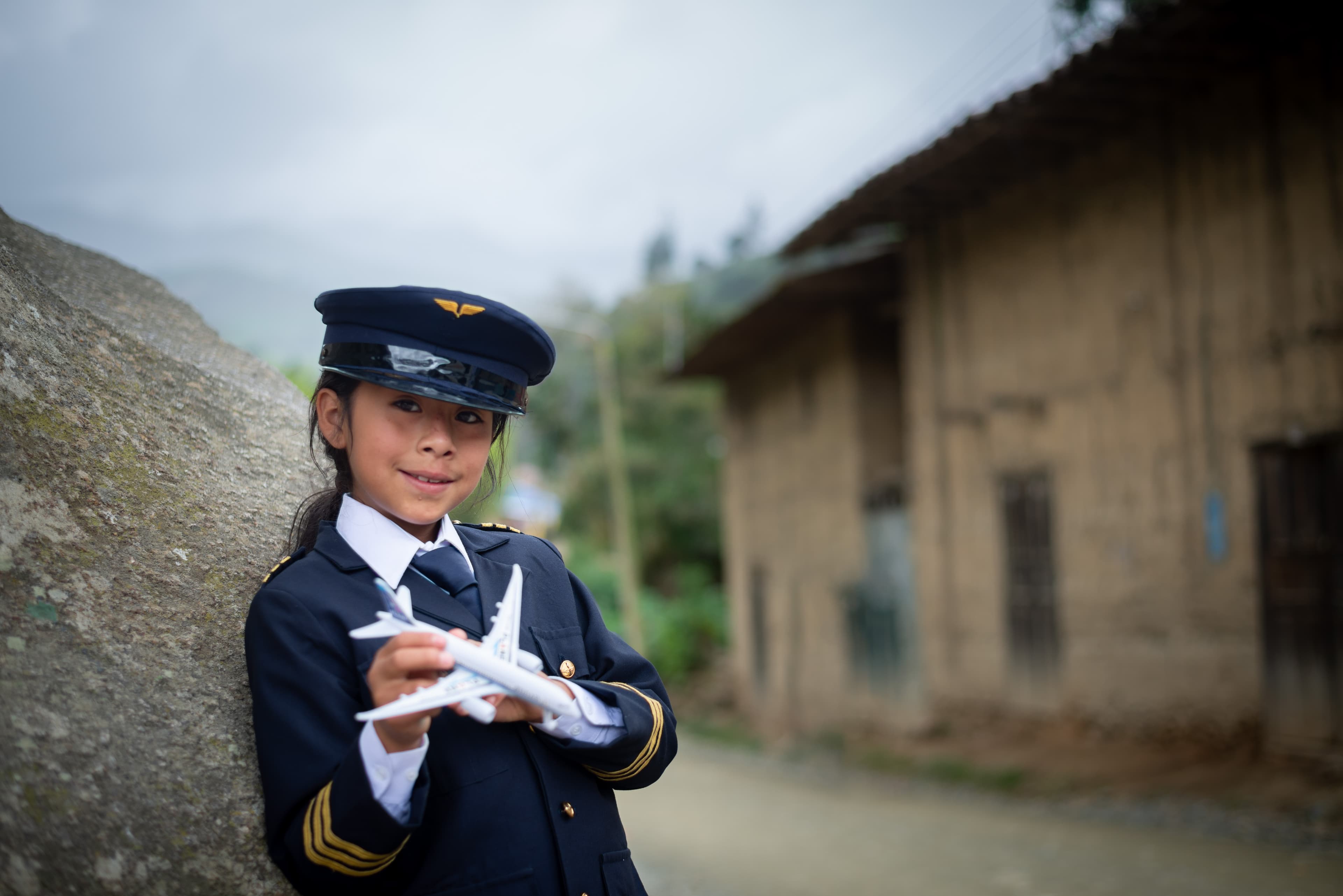 A young girl wearing a pilot costume holds a toy plane while smiling.