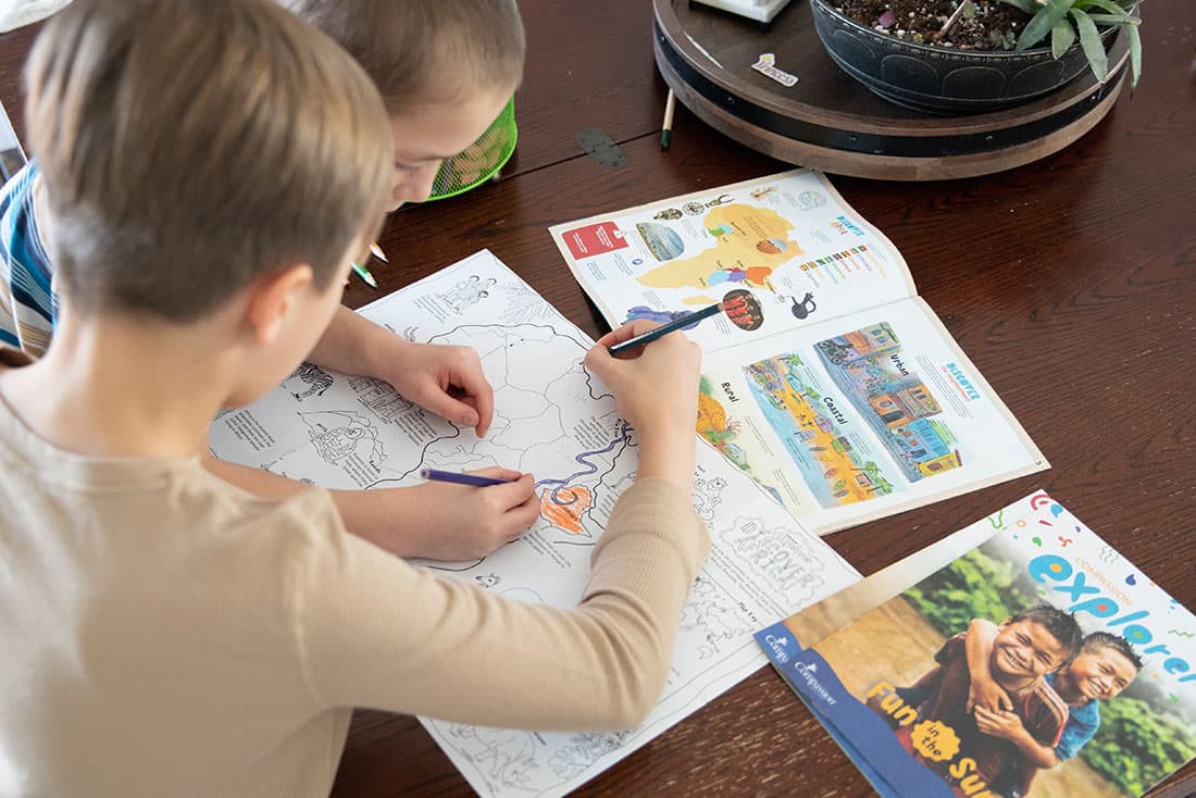 Two young boys sit at a table and color inside Compassion's Explorer Magazine
