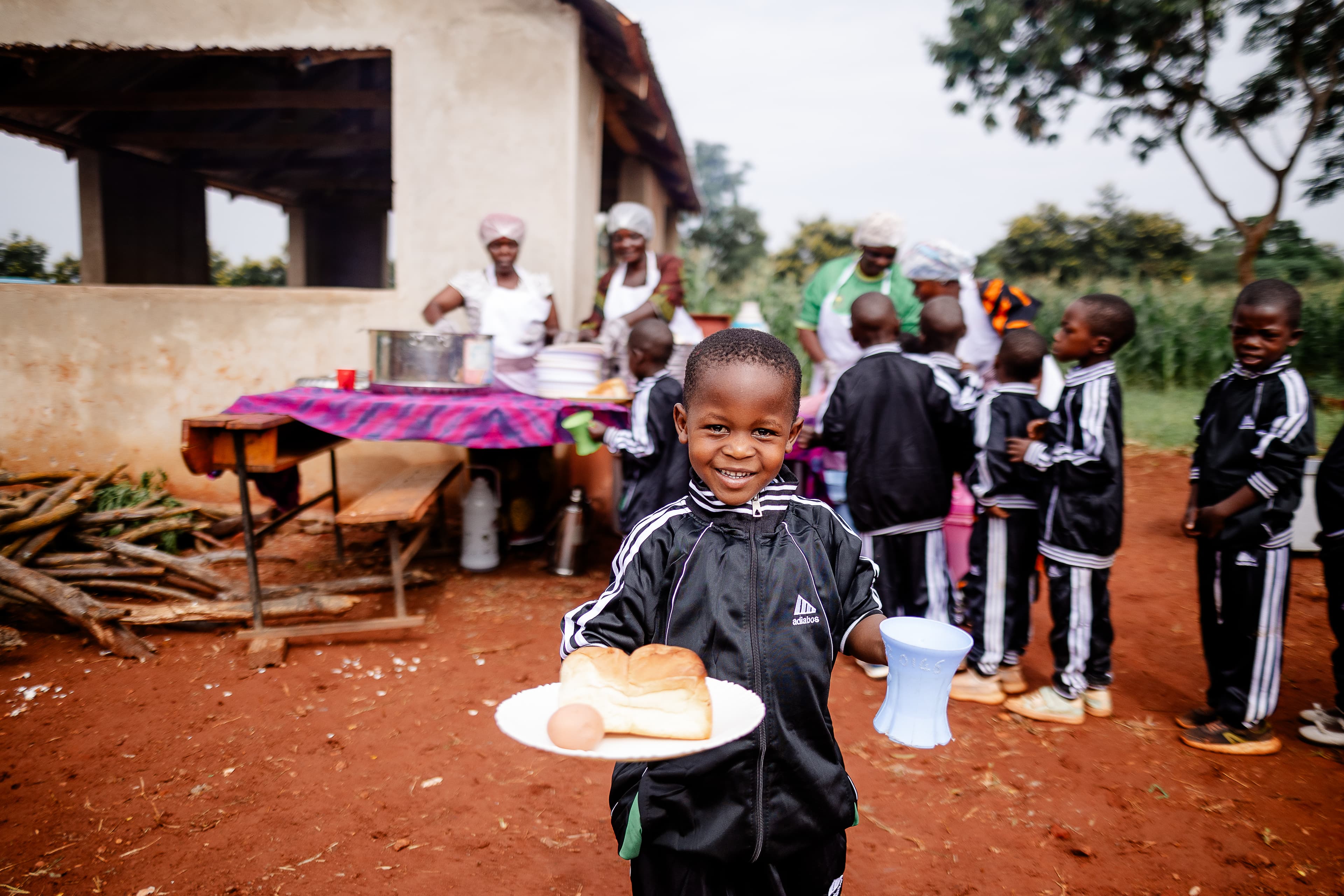 A young child is holding bread, eggs and tea while smiling at the camera.