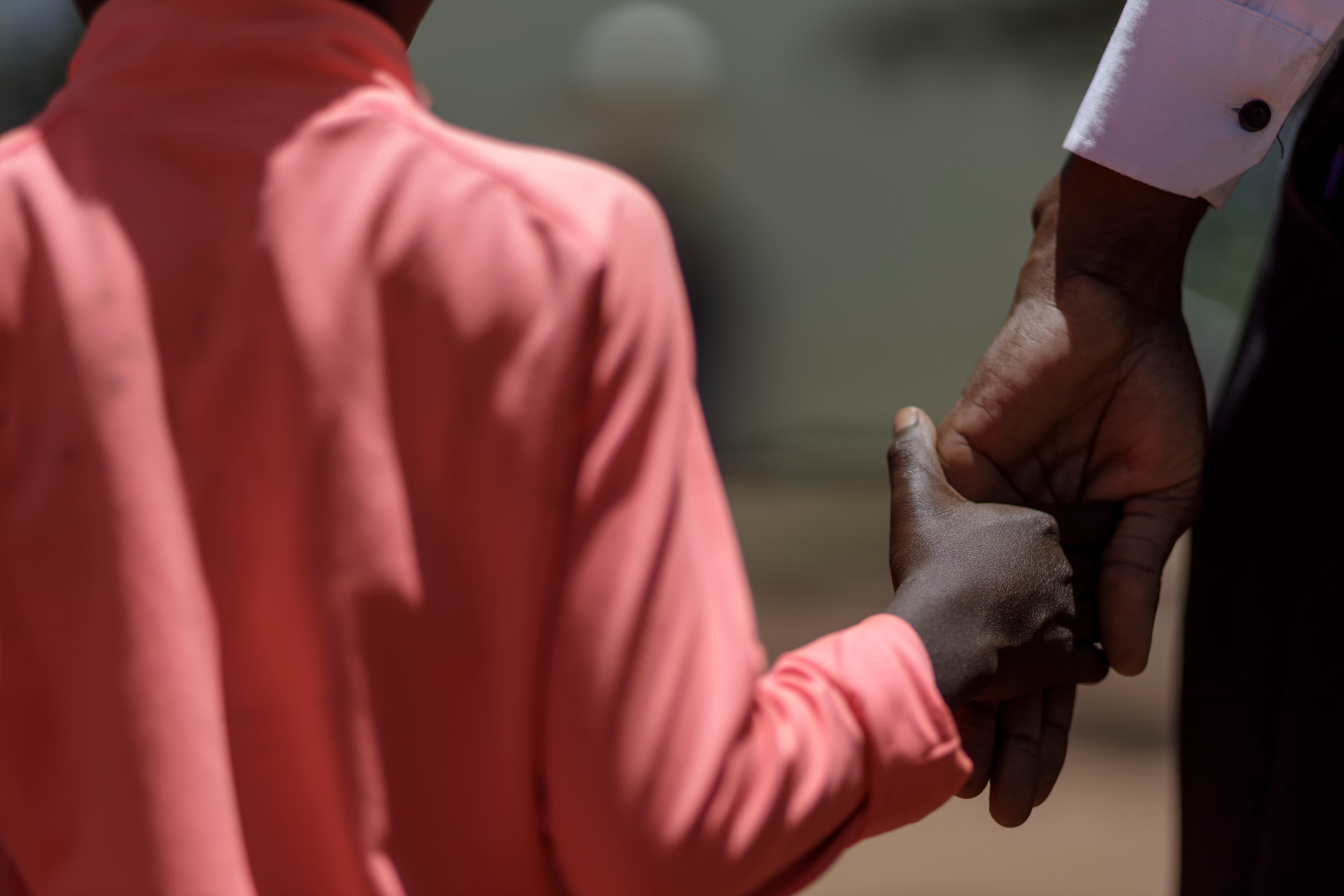 An up-close image of a child development worker holding a child’s hand.