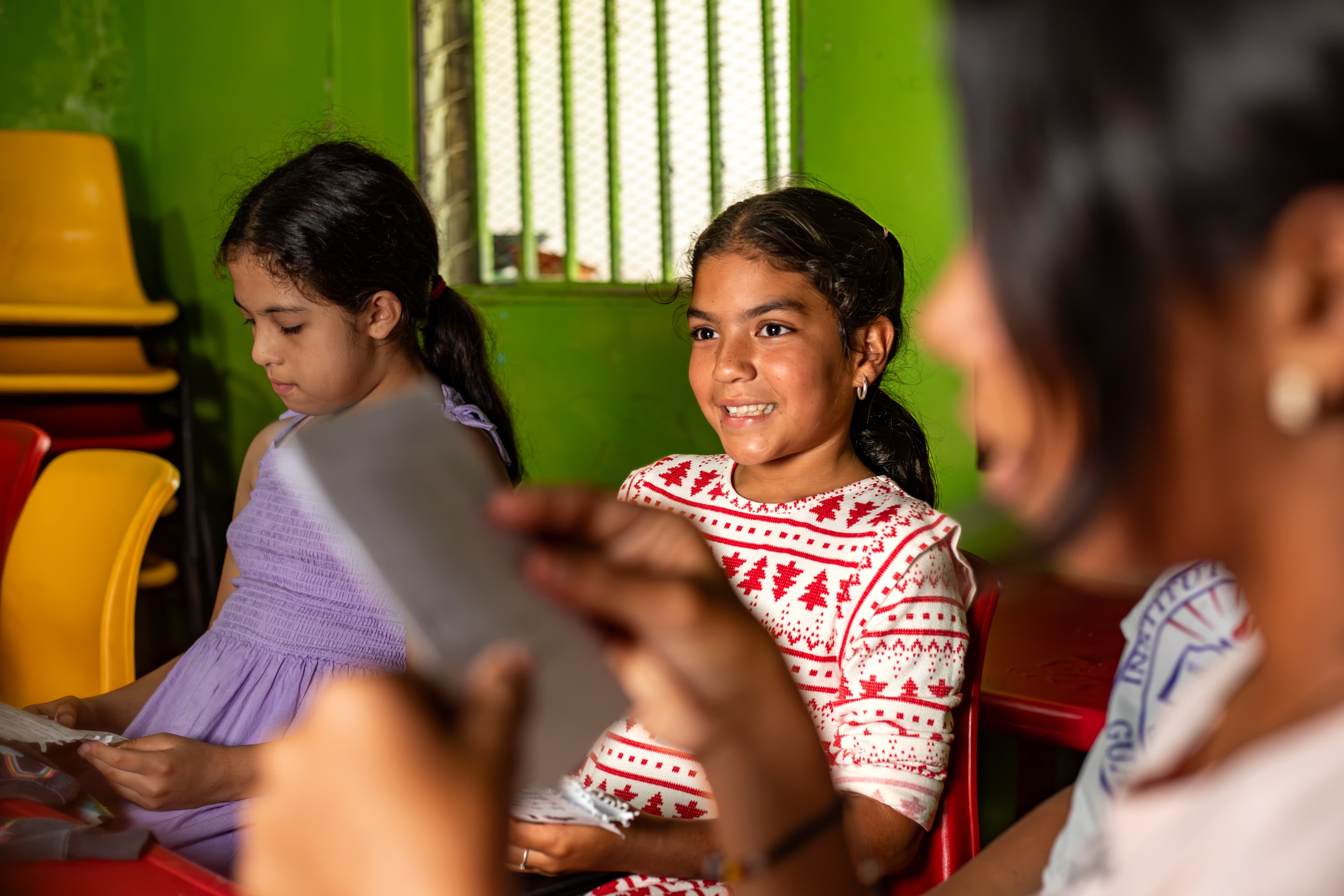A young girl is sitting in a classroom with students on both side smiling.