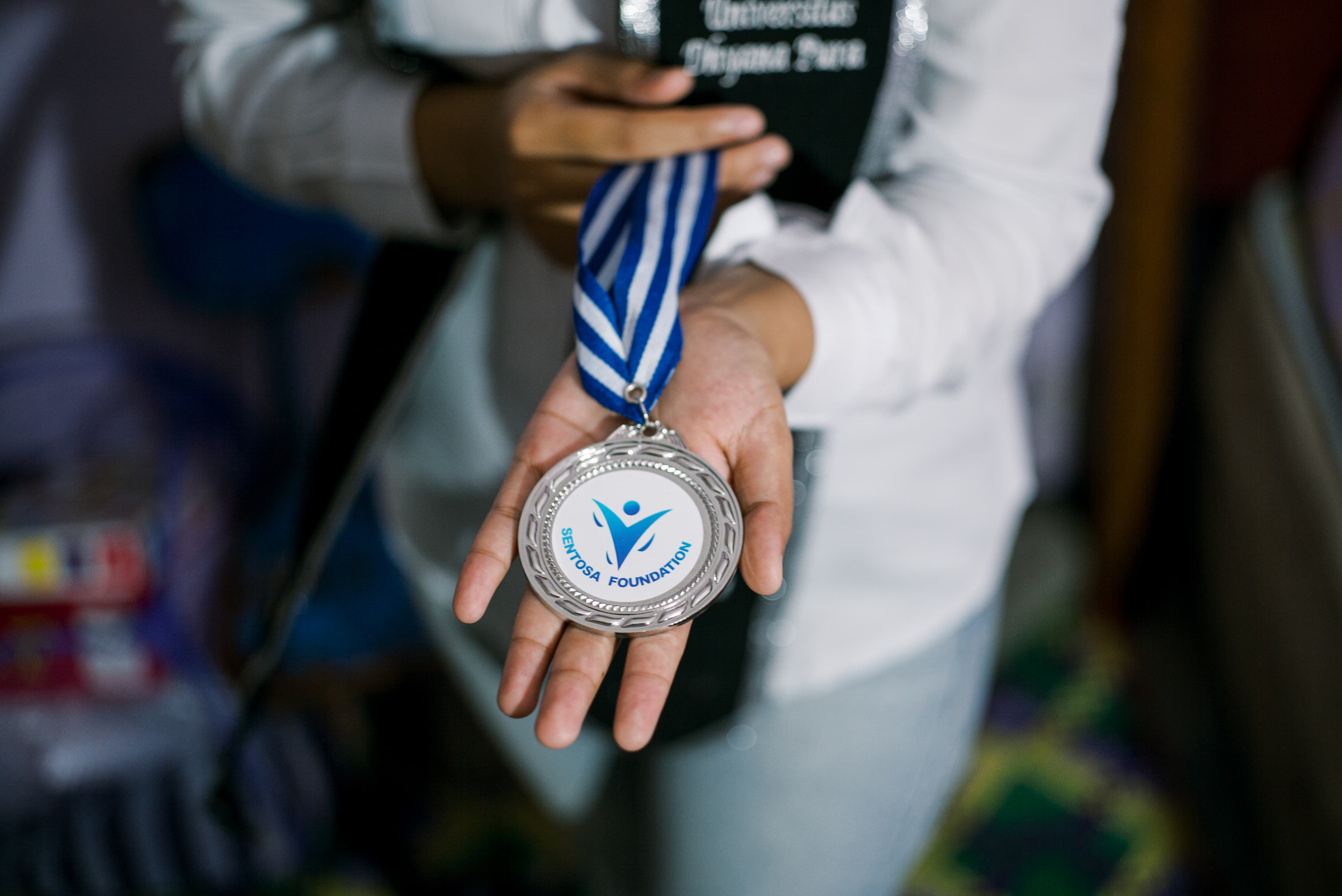 A young woman's hand holds up a silver medal.