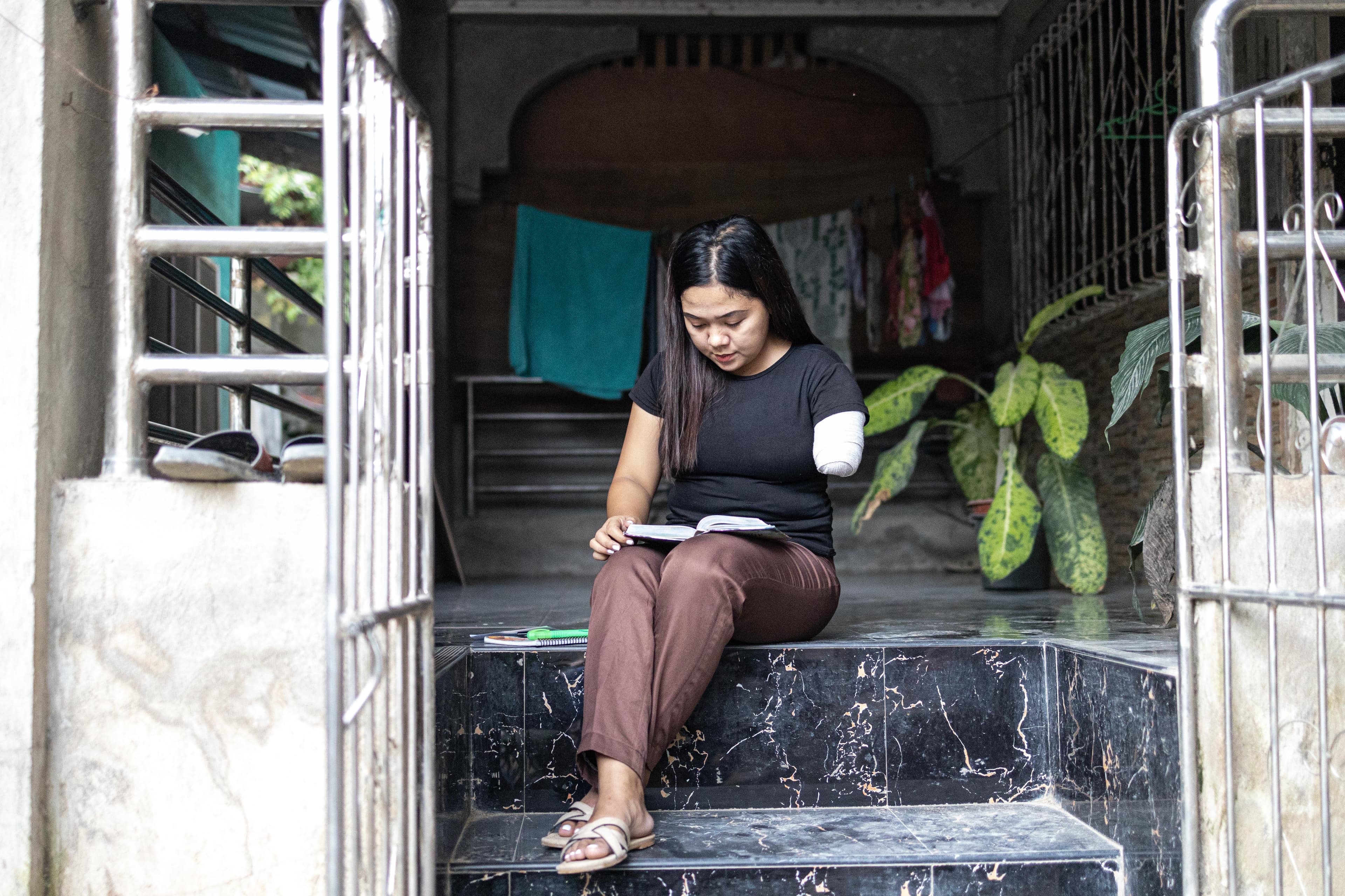 A young girl with a disability is sitting on a staircase reading smiling.