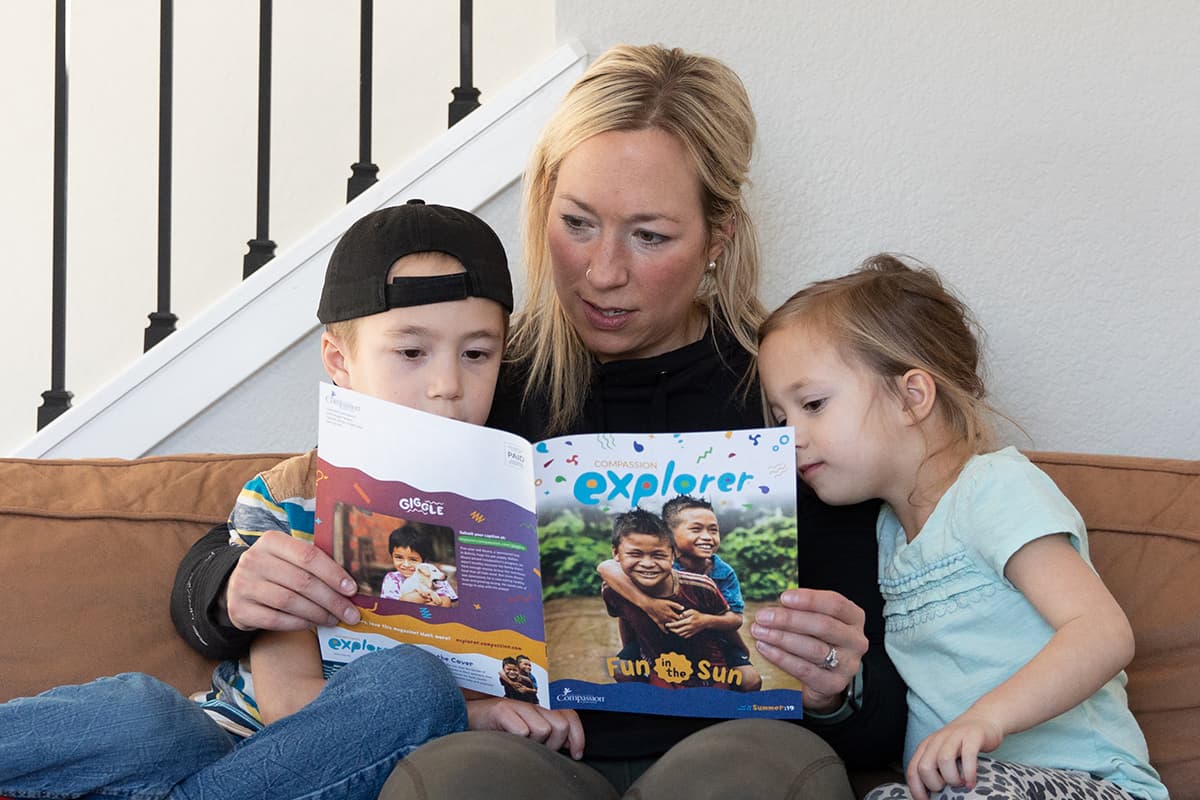 A mother sits with her two children reading a copy of Explorer Magazine.