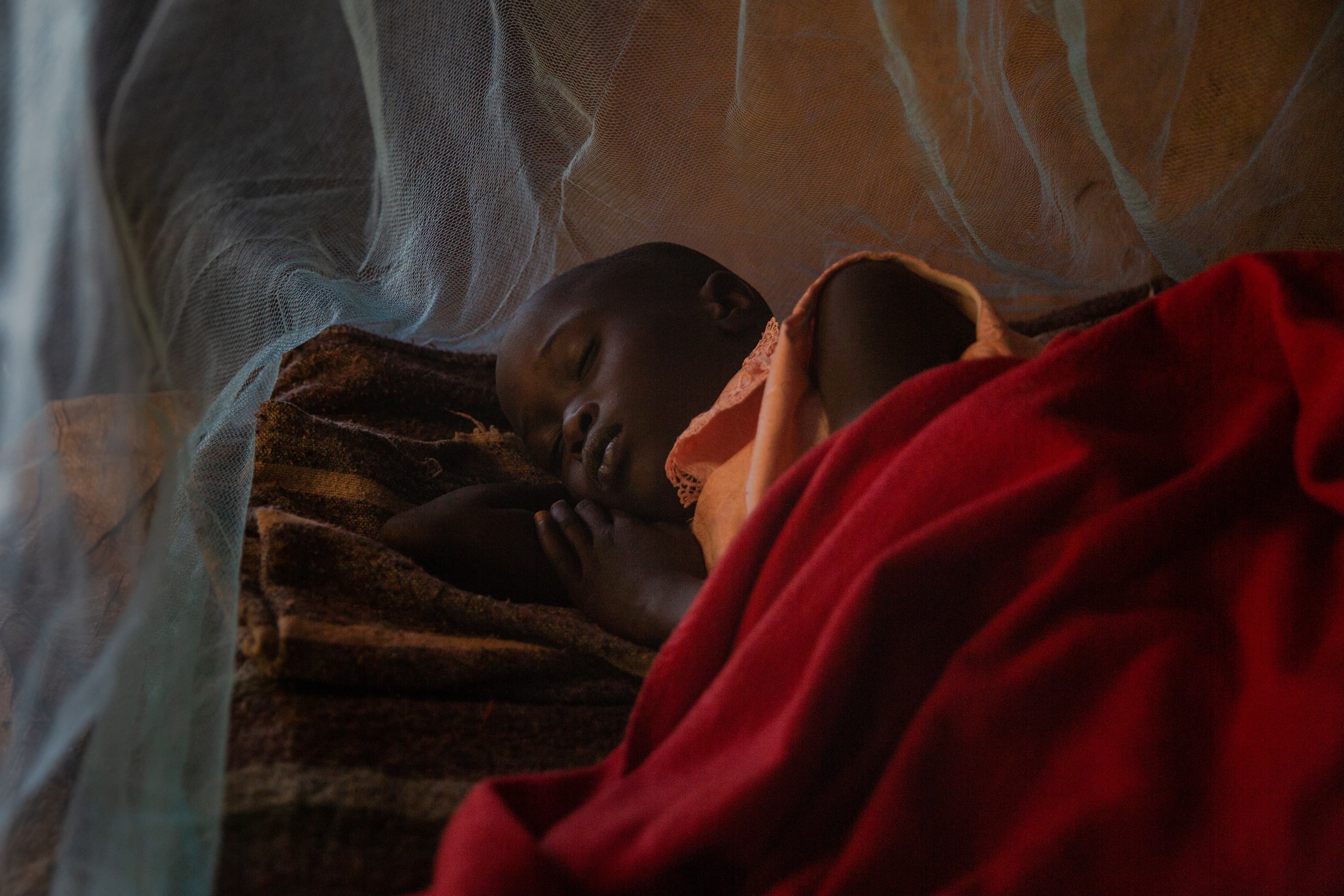 Young girl sleeps peacefully on a bed under a mosquito net.