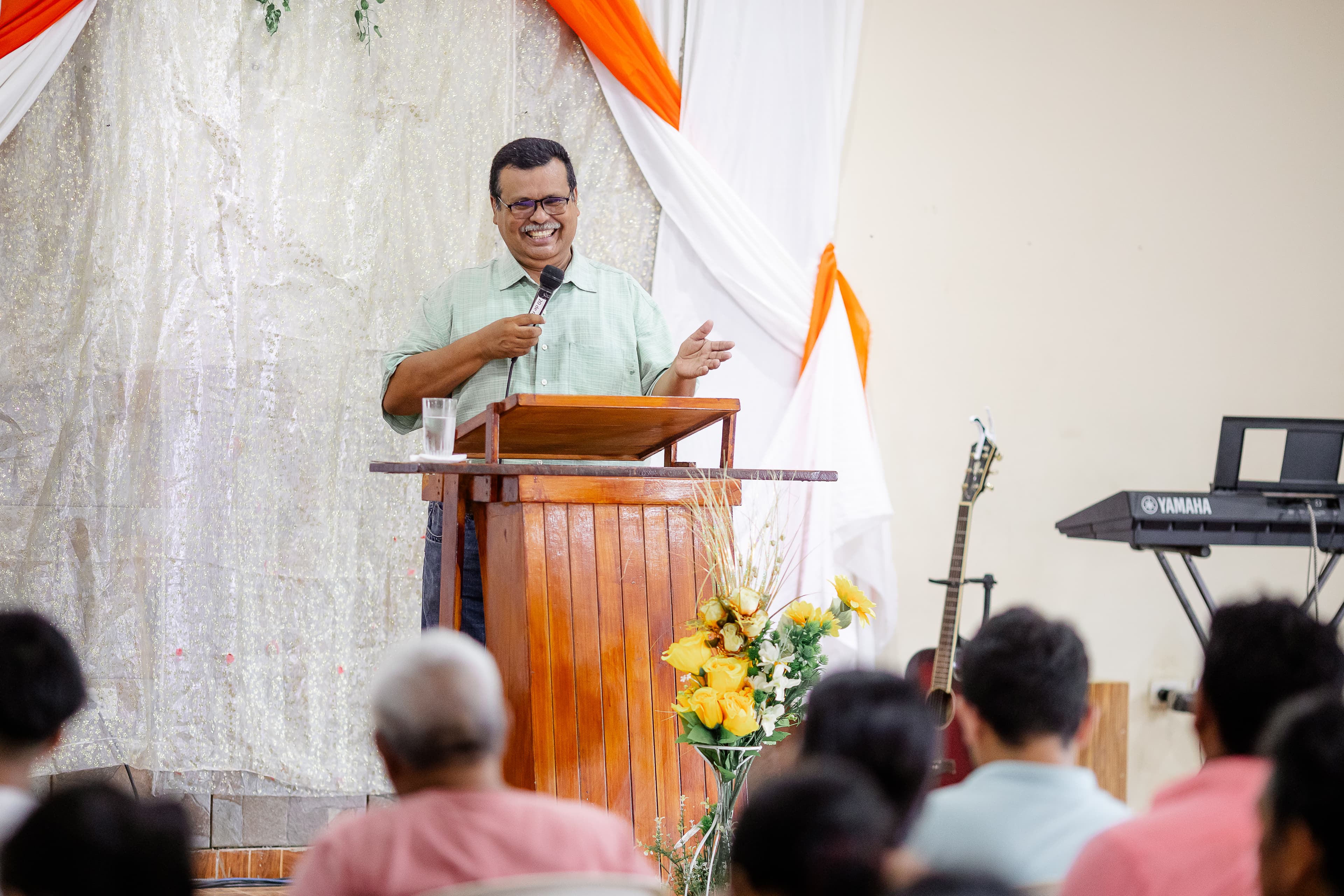 A pastor stands behind a pulpit holding a microphone and smiling.