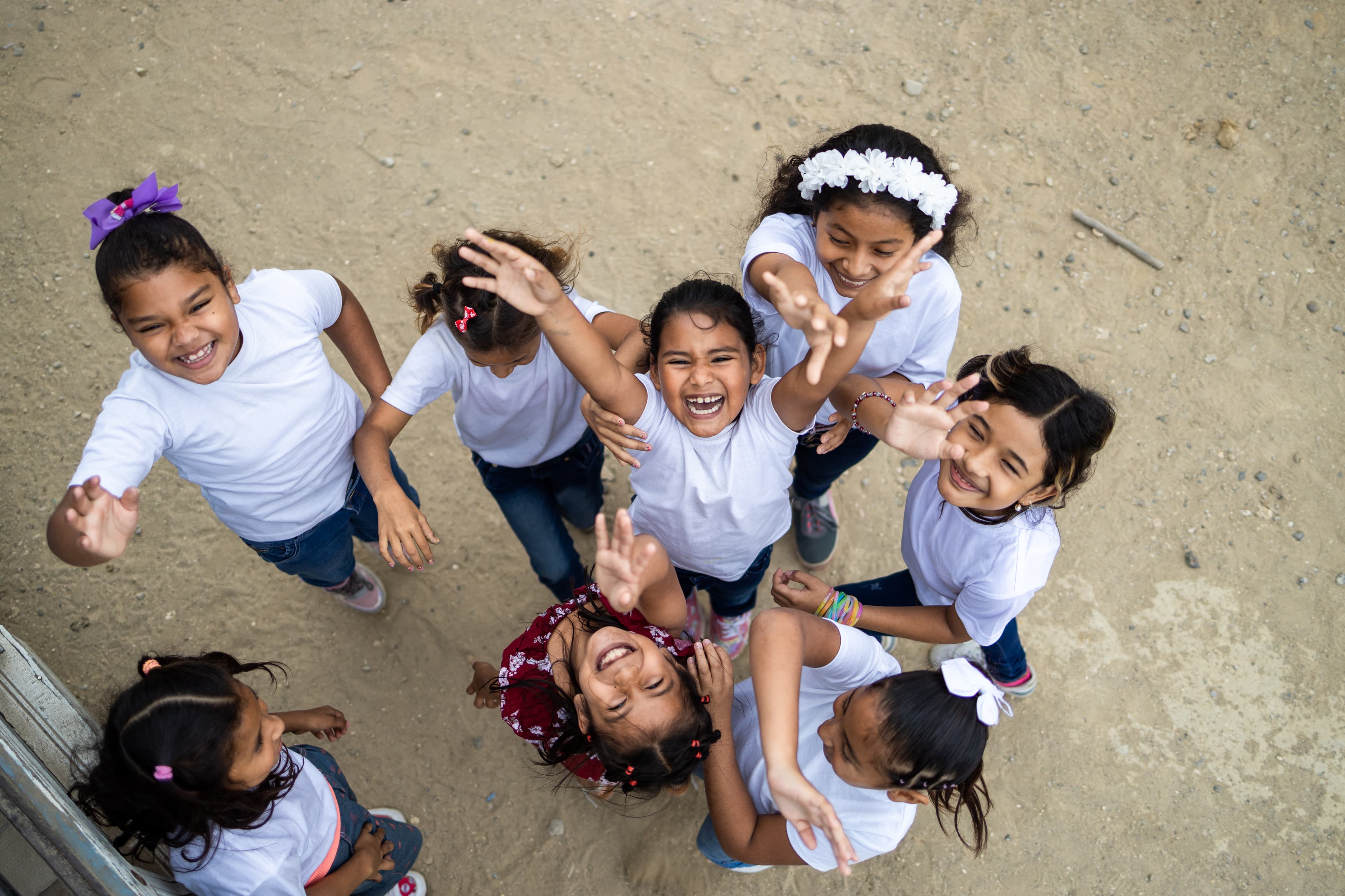 A group of girls wearing white t-shirts look up to the camera while smiling, dancing and laughing.