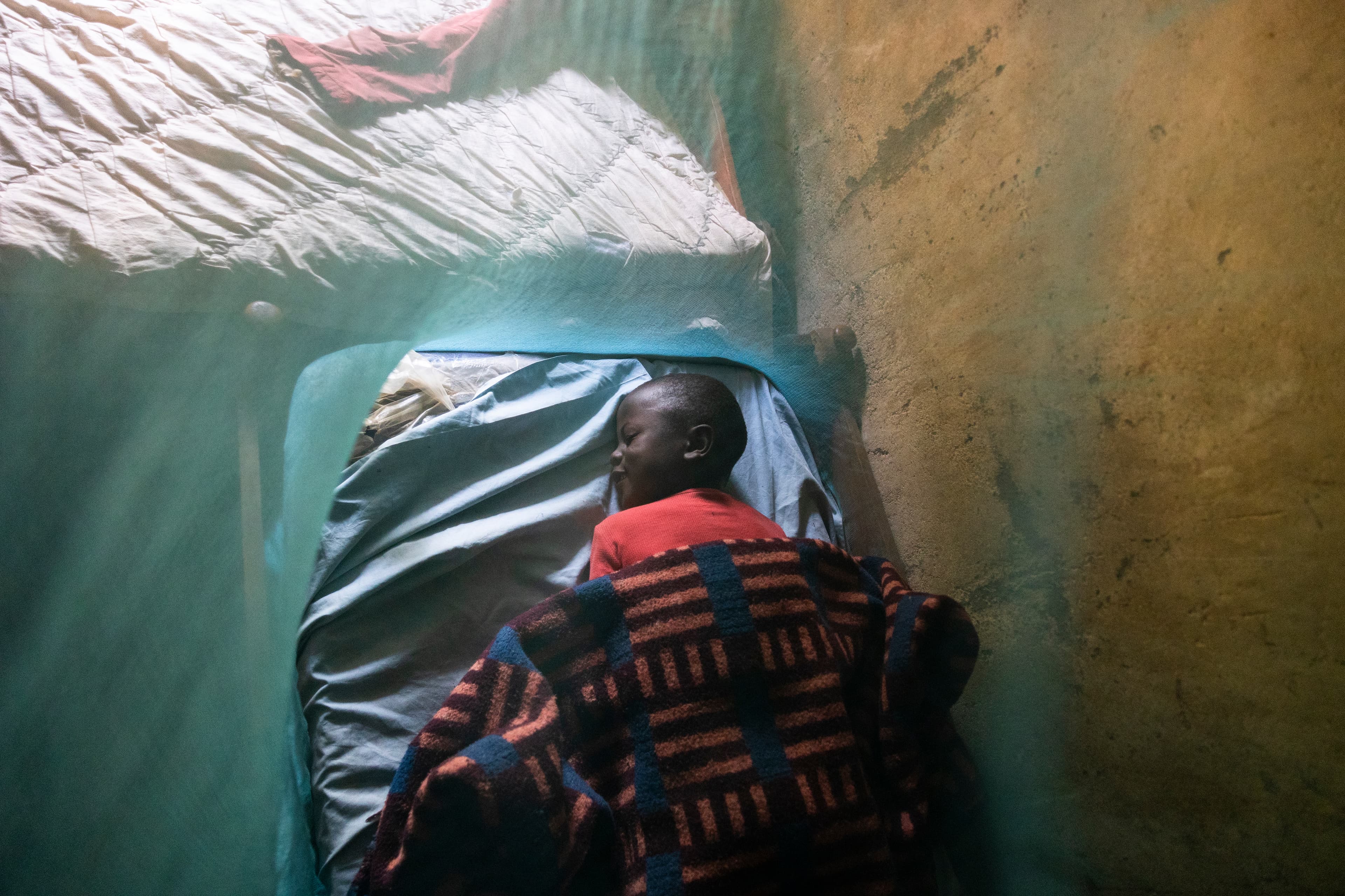 A young African boy sleeps on a bed surrounded by a mosquito net.