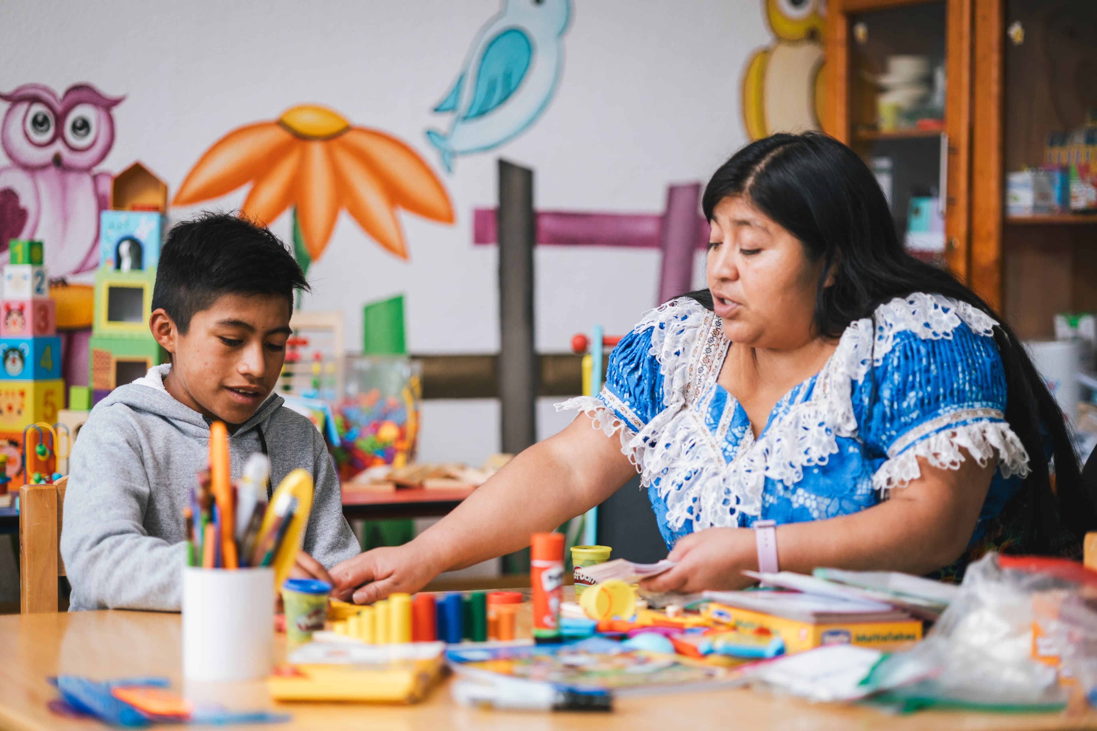 A Guatemalan tutor teaches a boy at a table full of school supplies.