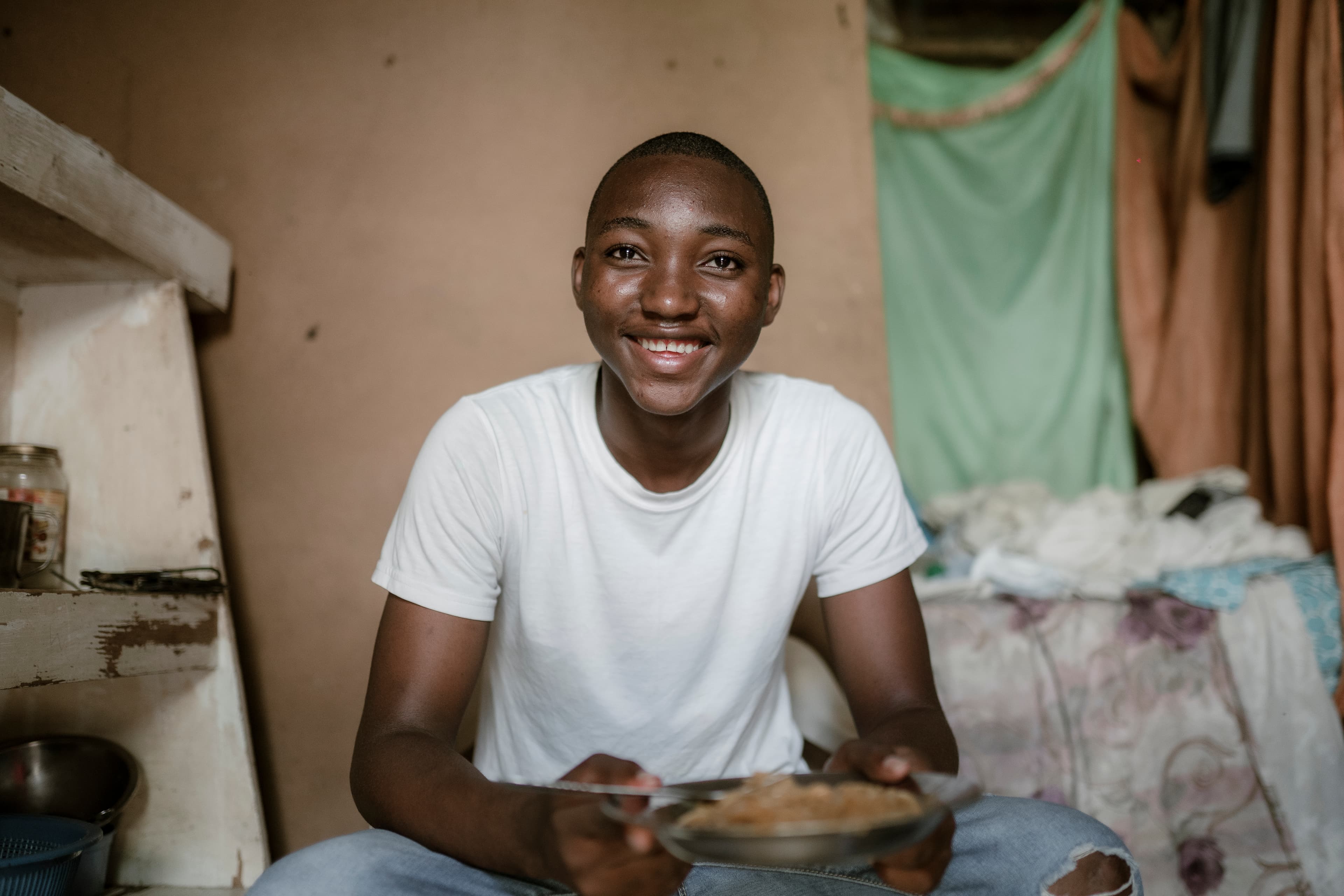 Young boy smiles as he sits on a chair eating a bowl of spaghetti.