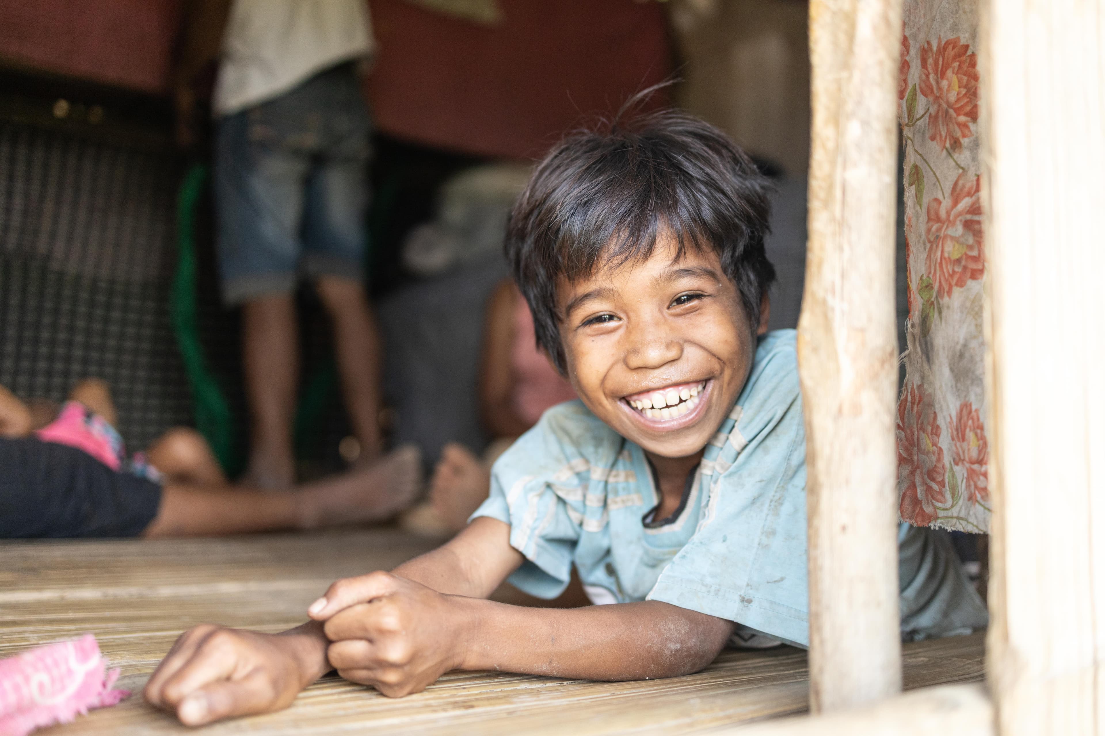 A young Filipino boy lays on the floor of his home while smiling brightly for the camera.