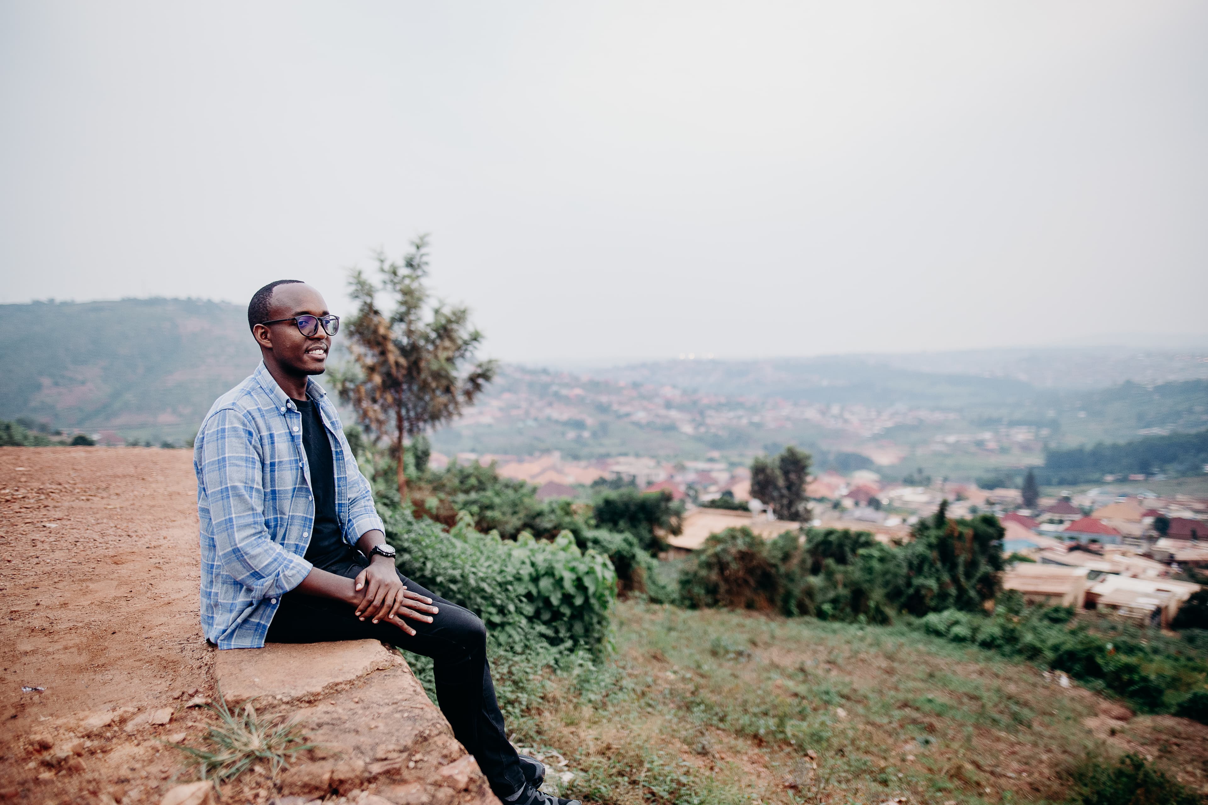 An African man sits on a ledge overlooking the hills in Rwanda.