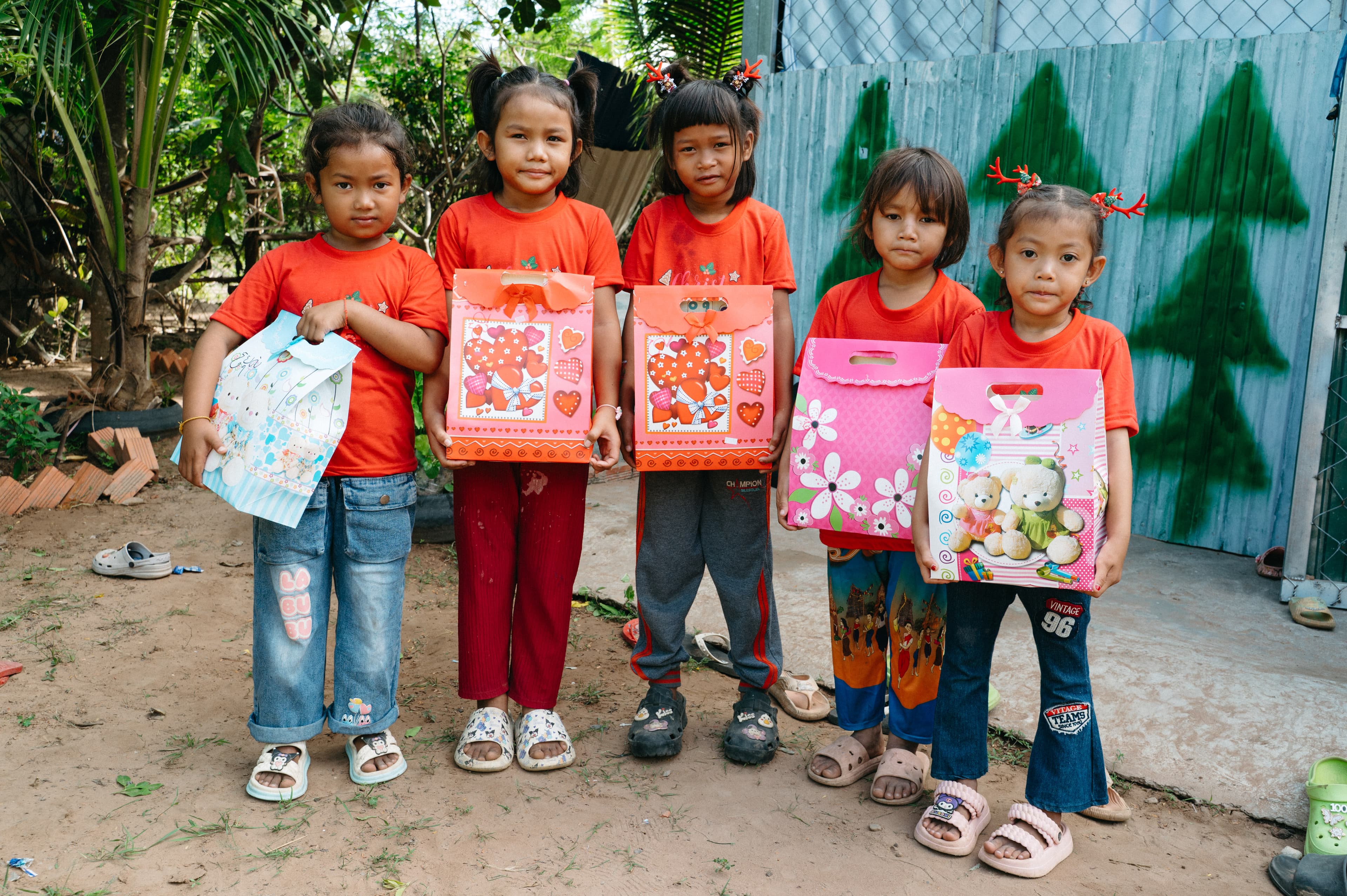 Young girls stand together in a group smiling while holding gifts.