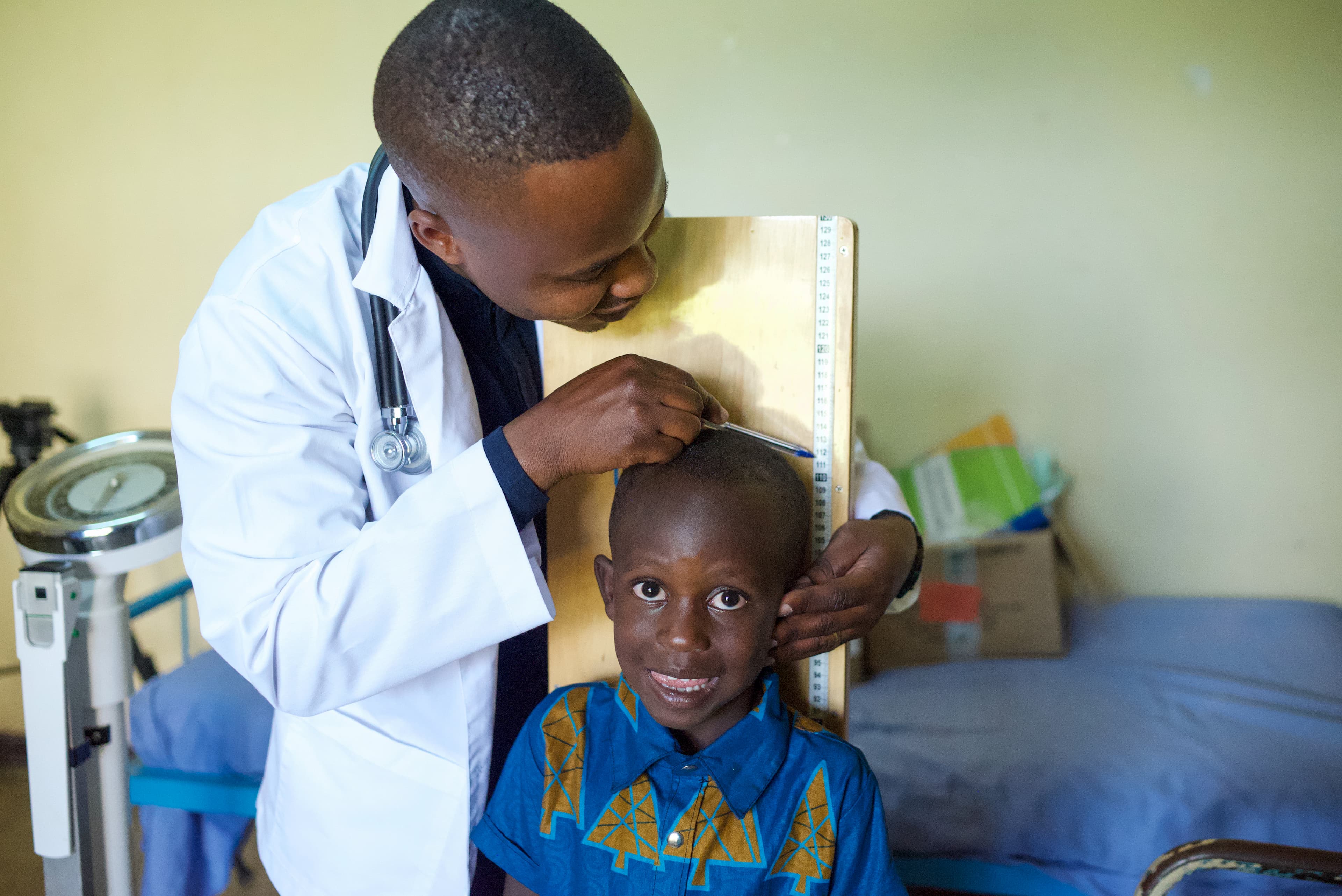 A young African boy is measured by a doctor wearing a white coat.