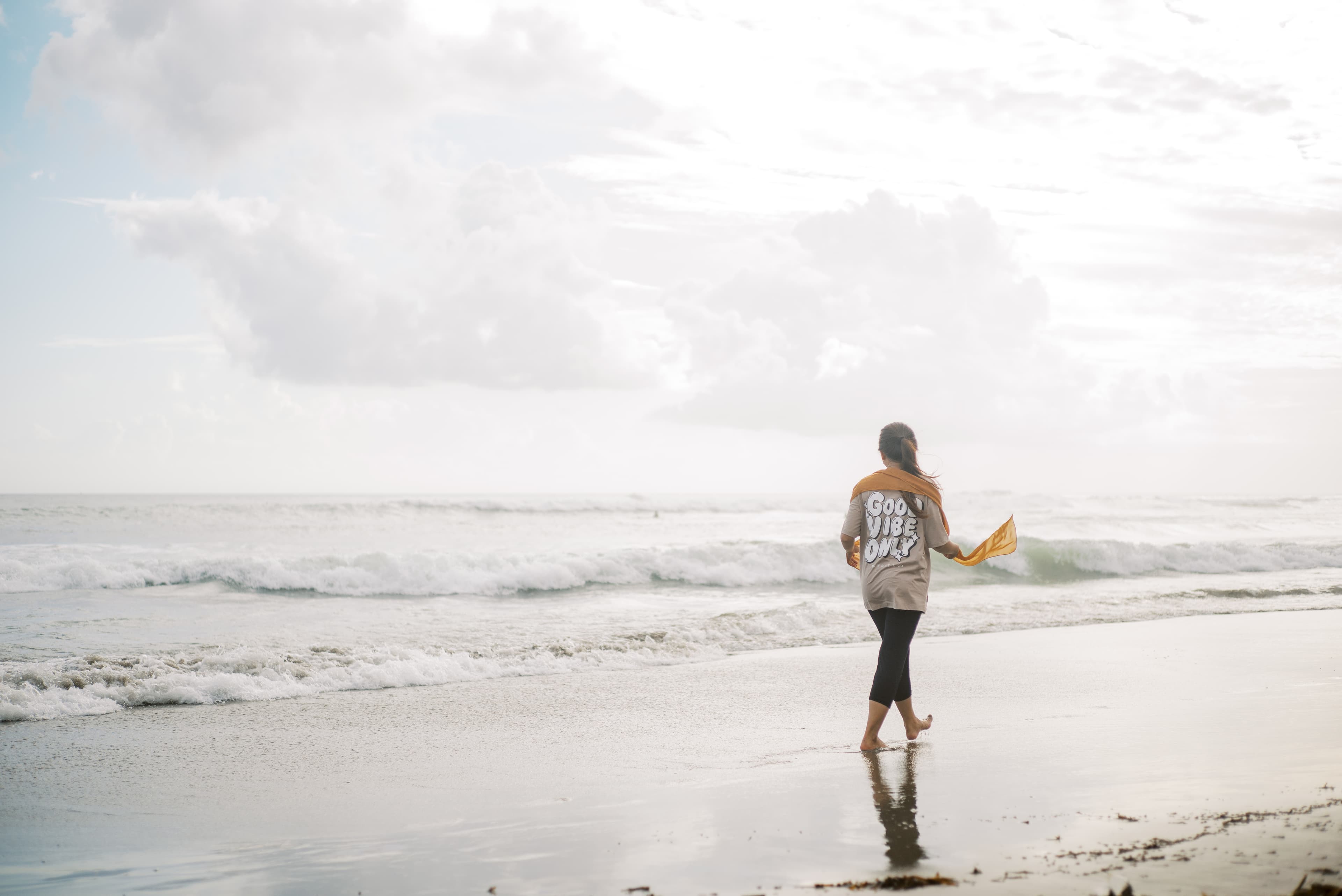 A teen Indonesian girl wearing a gold scarf walks on a beach in the water.