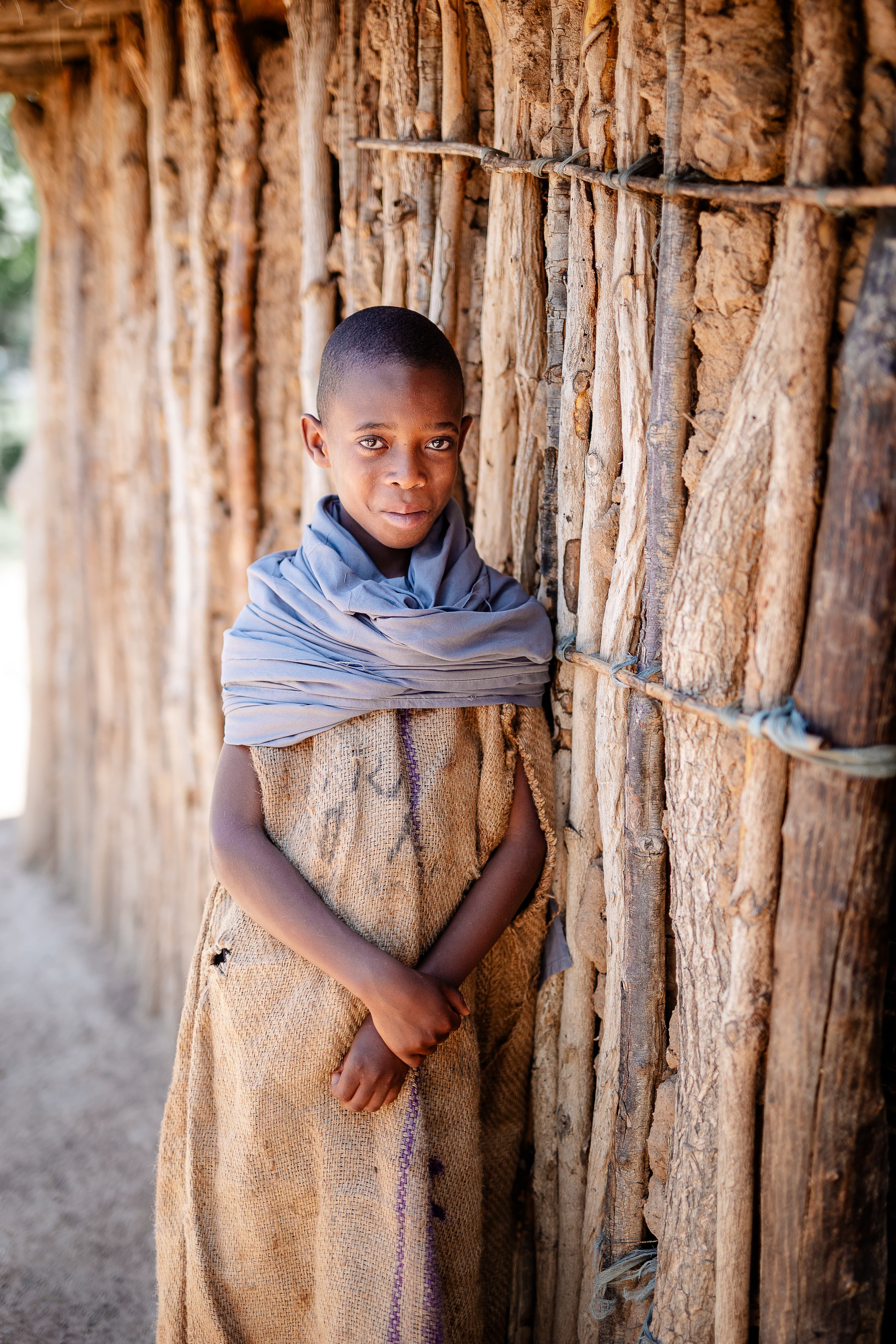 A young child is leaning against a wooden home with their arms crossed.