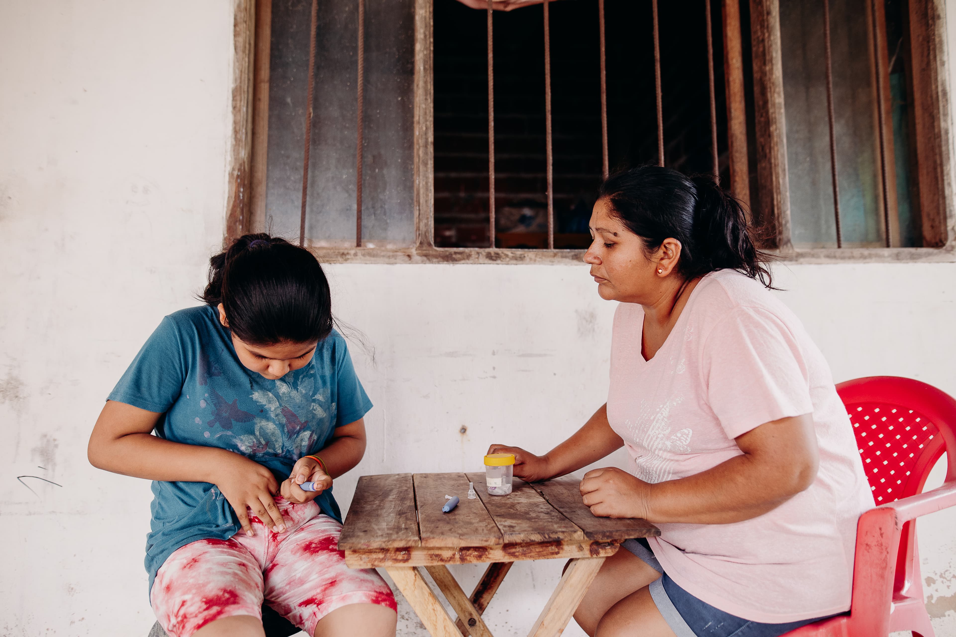 A young girl gives herself an insulin injection as her mother watches.