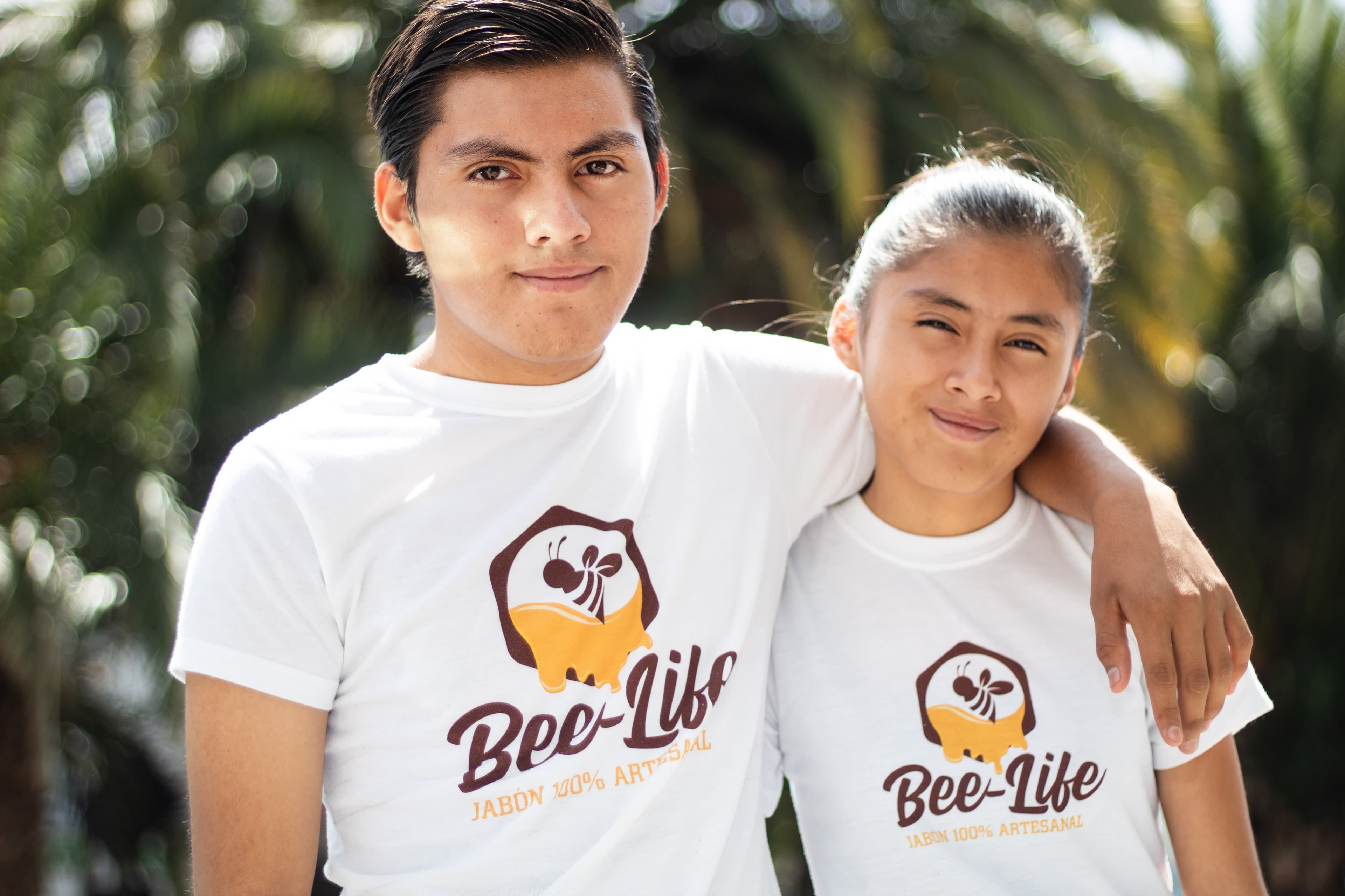 A brother has his arm around his sister as they stand in a park together.